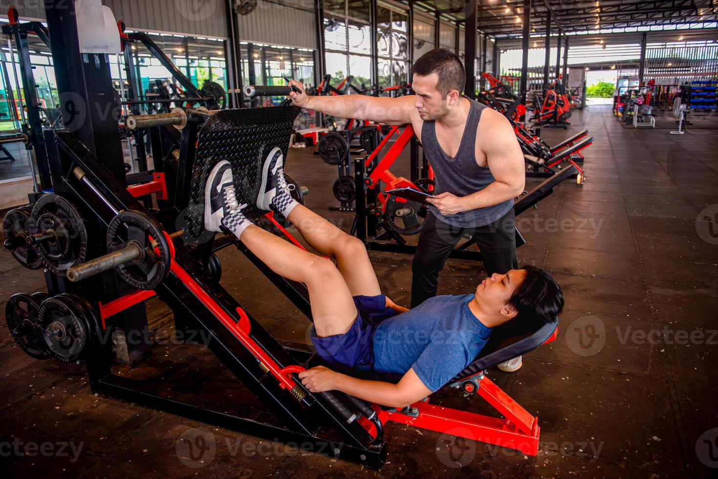A male trainer is helping his trainee use a leg press machine by pushing the handles of the machine. photo