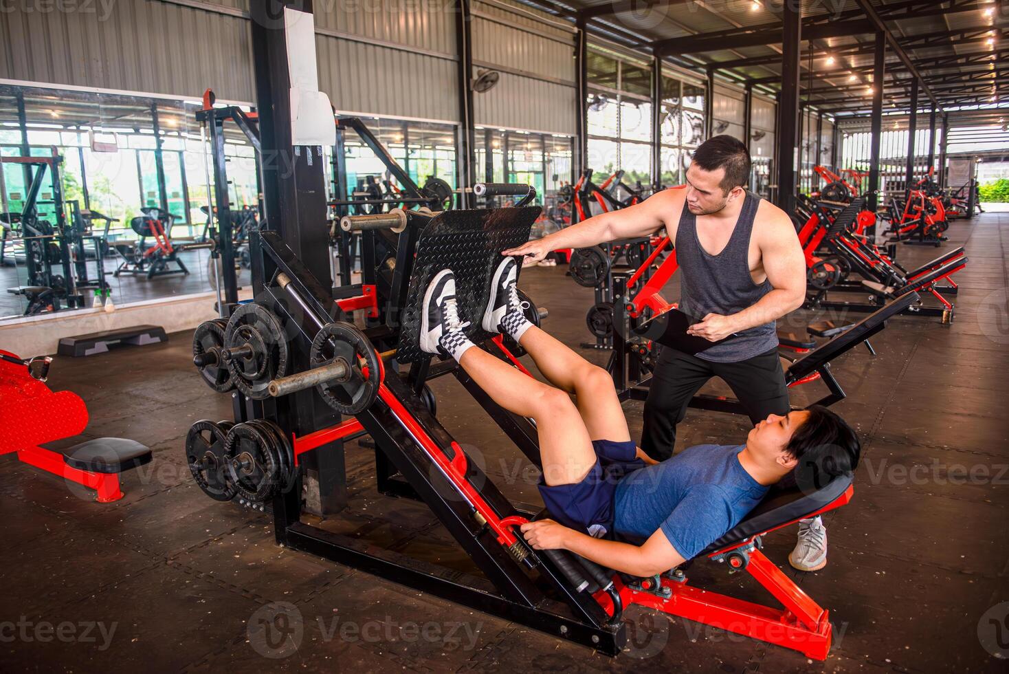 Male trainer advises proper foot placement when using the leg press machine in a fitness center. photo
