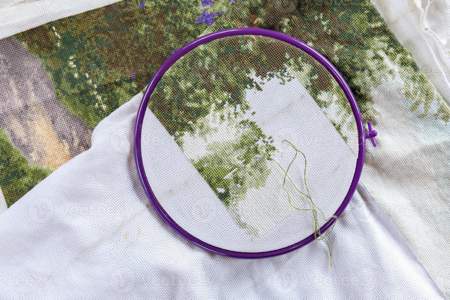 A girl cross-stitching. Close-up of hands carefully maneuvering a needle through the fabric. A purple embroidery hoop holds the fabric. Close-up of hands with a needle threading the fabric. photo