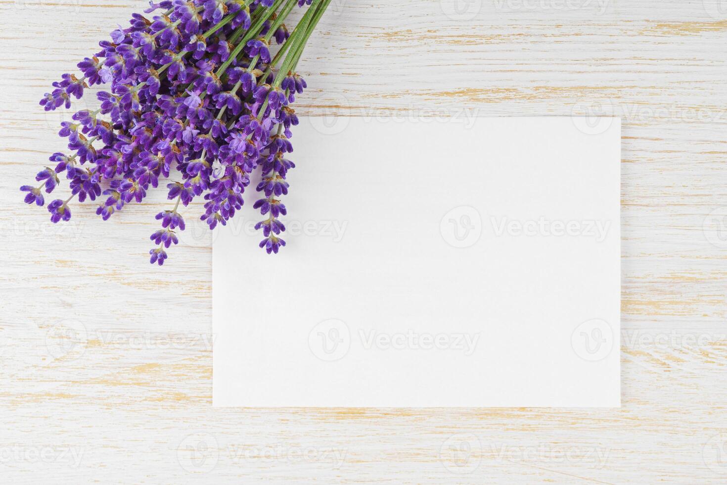 Bouquet of blooming lavender flowers on white wooden surface with rectangular blank sheet of paper photo