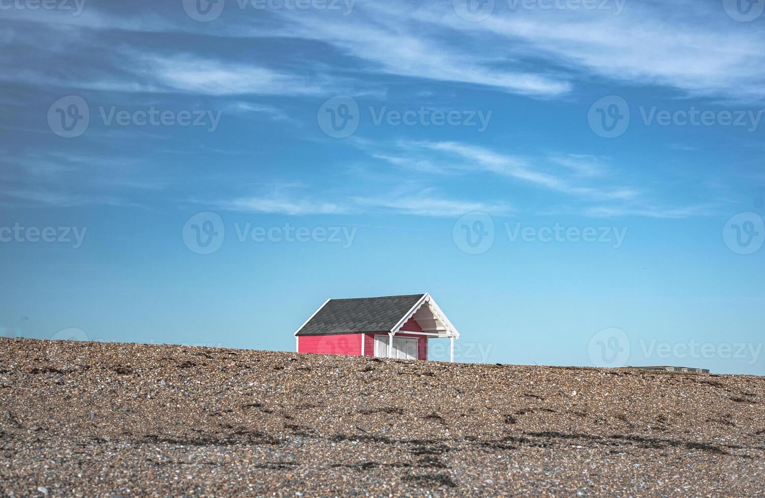 Single little cabin hiding behind pebble dune on a beach of Lancin, West Sussex, UK photo