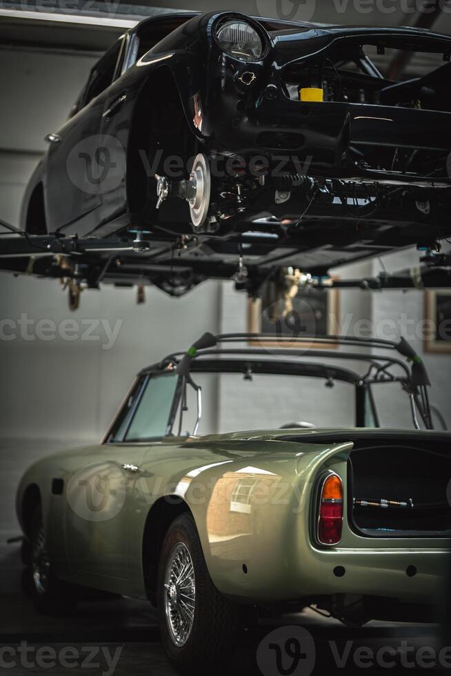 Classic, vintage, British car being restored on a ramp with visible rear axle and stripped car underneath photo