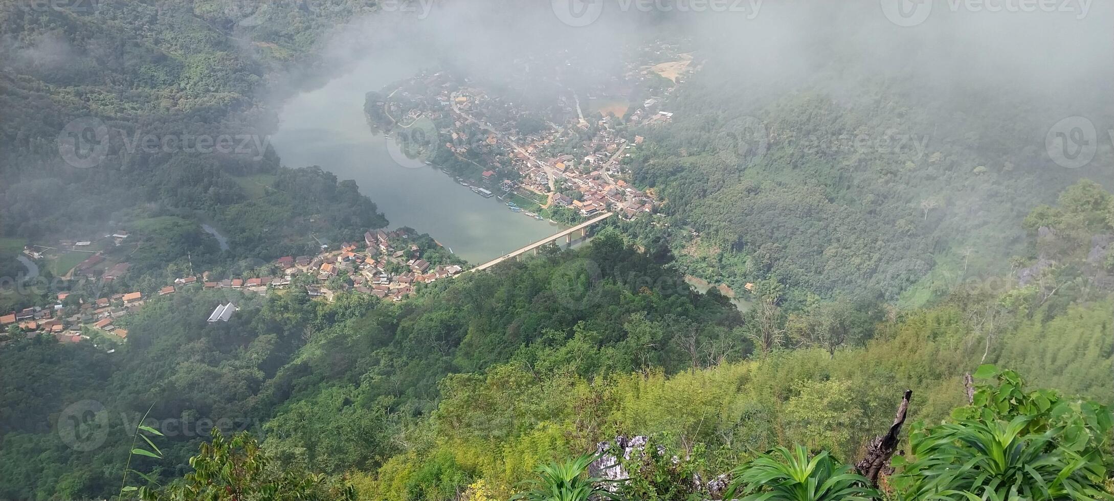 Aerial view of a foggy valley with a river, surrounded by lush green mountains and a small village. photo