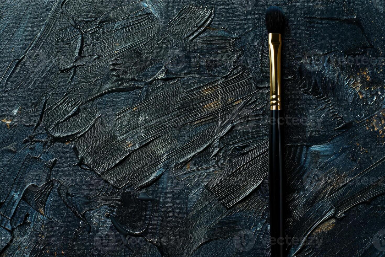 Makeup brush laying on textured black and gold painted background photo