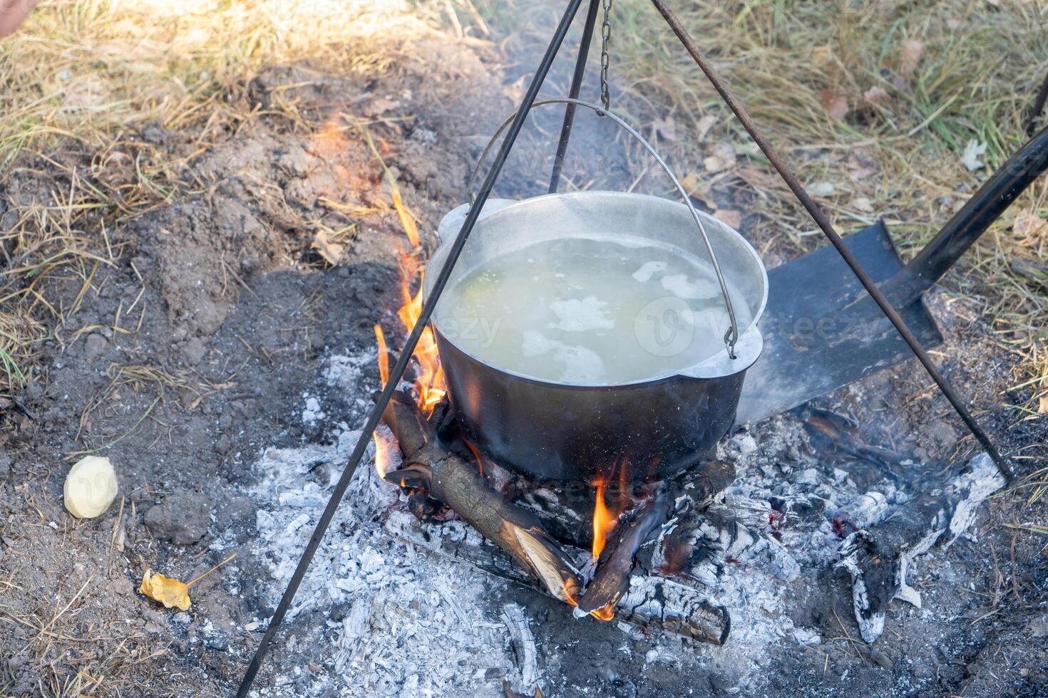 Cook porridge on a hike. Add firewood and coals with a shovel. Cooking food on a campfire while hiking. Soup in a cauldron outdoors. Camping and tourism. photo