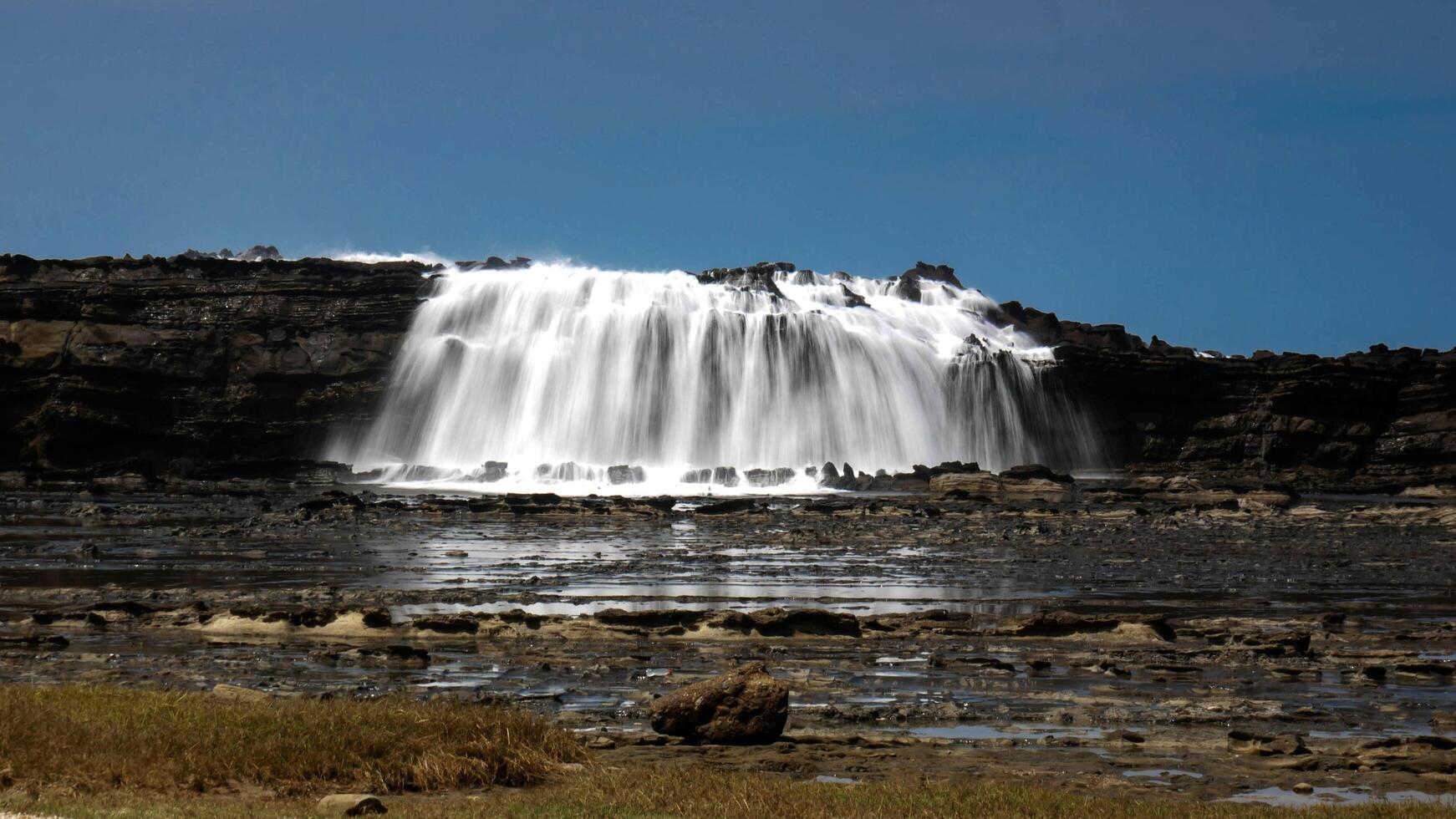 Big waves create beautiful sea views of waterfalls and water flows in Karang Taraje, Sawarna Beach, Indonesia. A favorite location for domestic and foreign photographers to hunt for photos and videos.