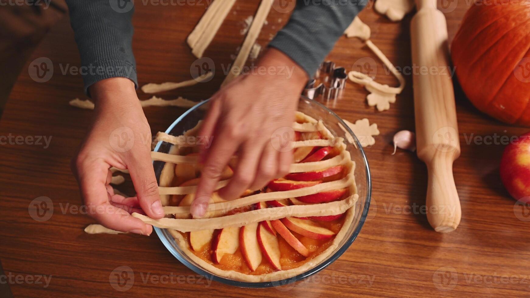 Hands creating a homemade pumpkin pie with lattice crust in a cozy kitchen setting photo