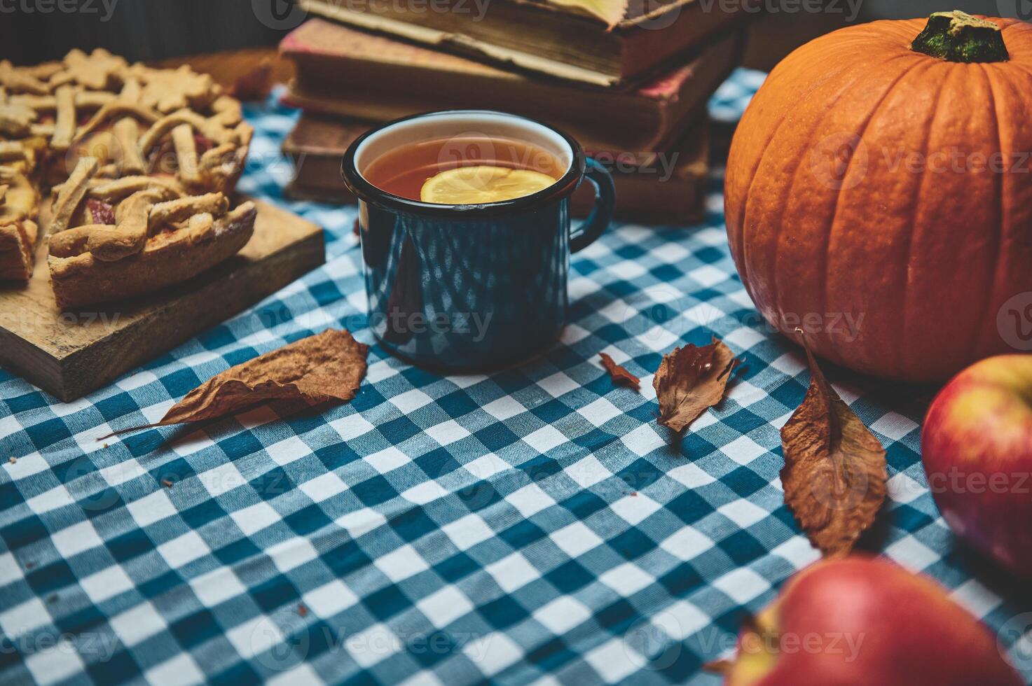 Cozy autumn scene with traditional apple pie, pumpkin, and hot tea on a checkered tablecloth capturing the warm, inviting essence of the fall season. Perfect for Thanksgiving and autumnal gatherings. photo
