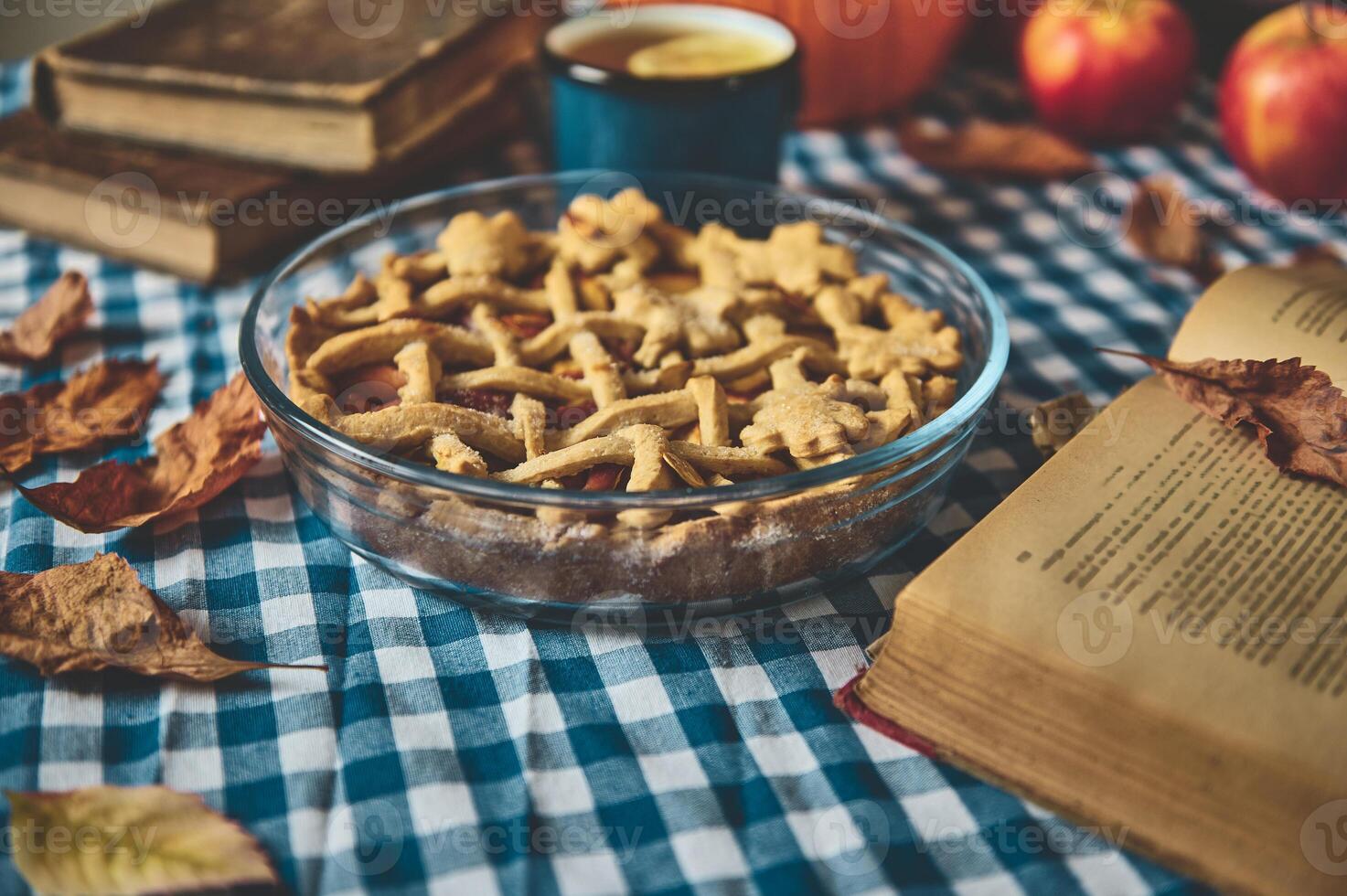 Cozy autumn scene with homemade apple pie accompanied by a hot drink and books, set on a checkered tablecloth for a warm, inviting setting perfect for a fall afternoon relaxation. photo