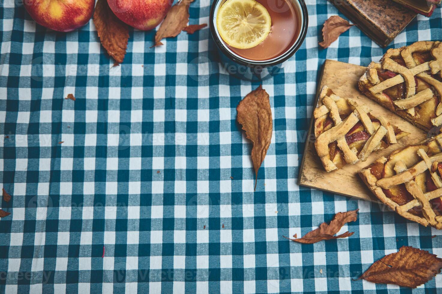 Autumn picnic table setting with homemade apple pie, warm tea, and fresh apples on blue checkered cloth photo