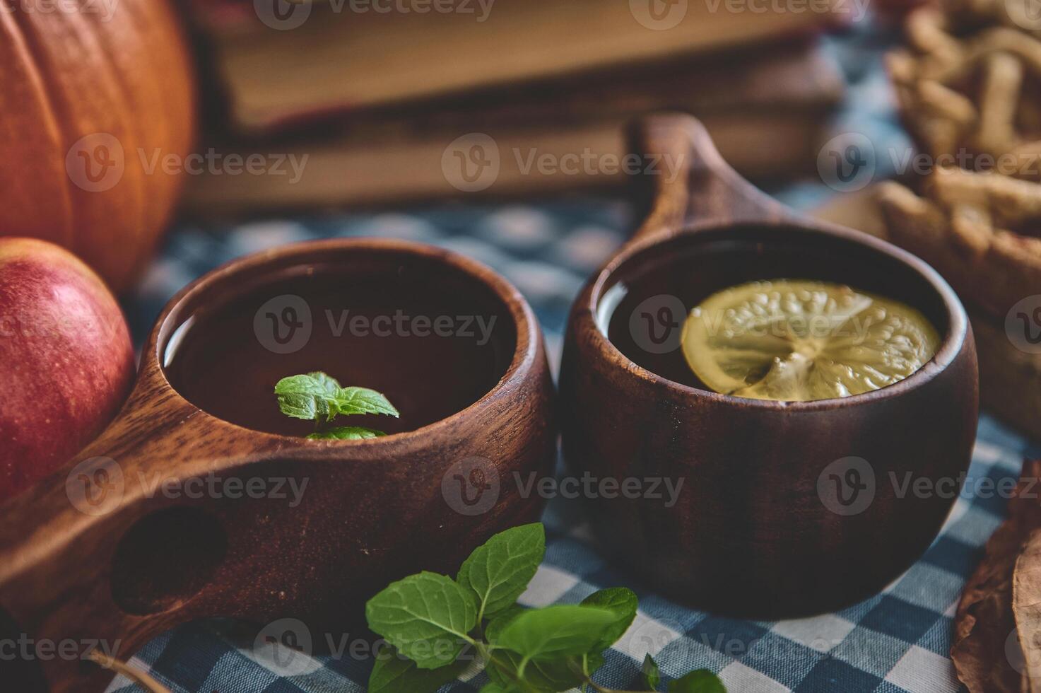 Rustic autumn drinks in wooden cups adorned with mint and lemon, set on a cozy gingham tablecloth with a backdrop of apples and pumpkin, creating an inviting harvest festival atmosphere. photo