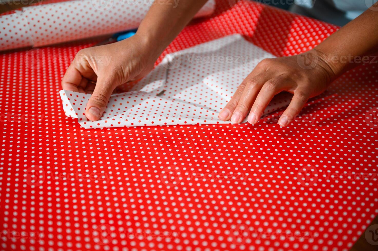 Hands carefully folding polka dot wrapping paper in preparation for gift wrapping, creating a beautifully wrapped present with precision and attention to detail for a special occasion or event. photo