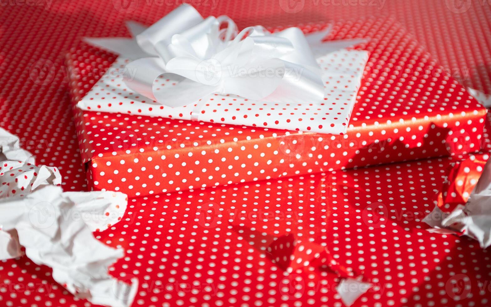 Festive polka dot gift boxes with white ribbons and crumpled wrapping paper on a red patterned surface photo