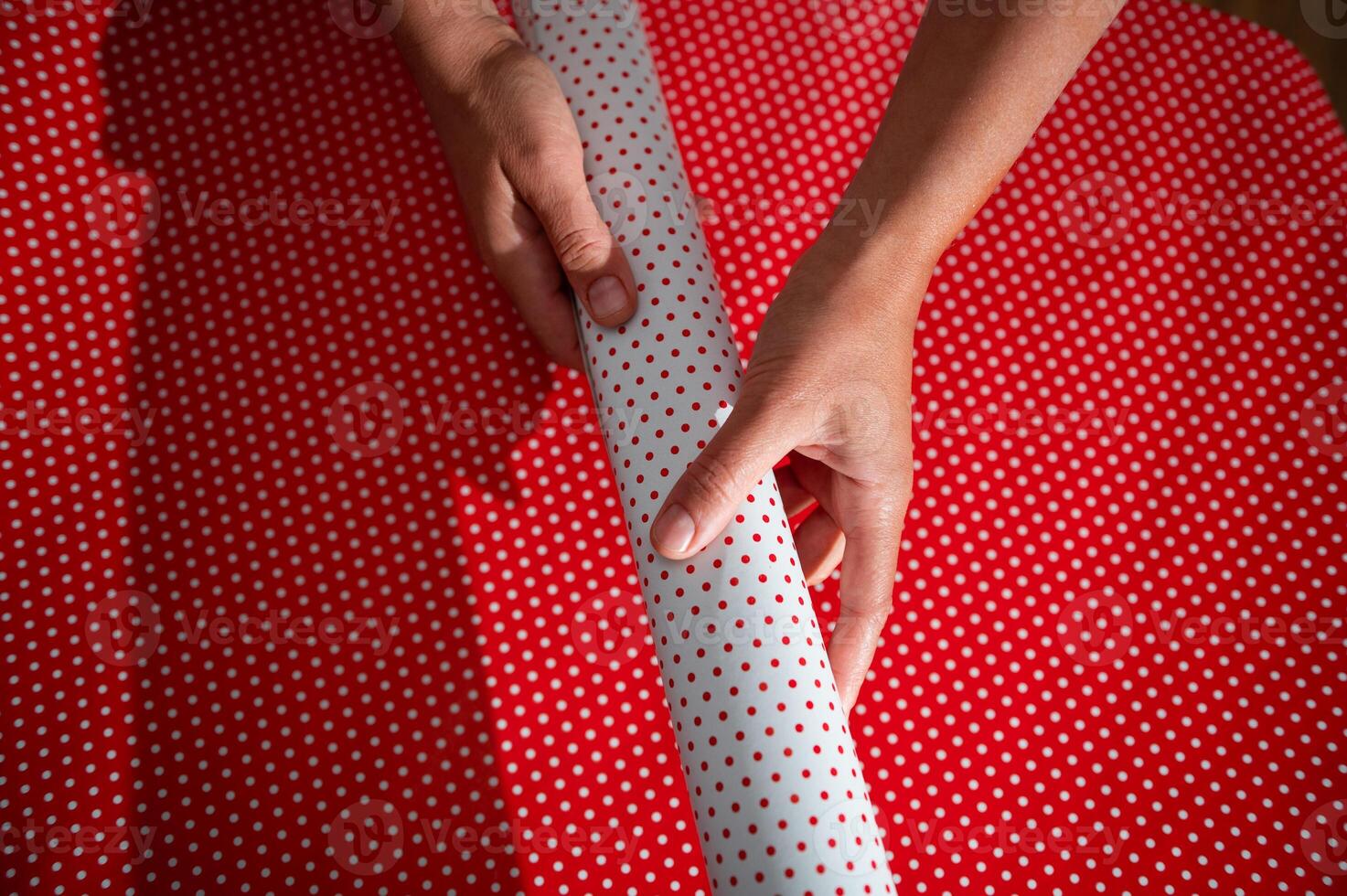 Hands holding and preparing red polka dot wrapping paper for gift on a festive occasion, symbolizing celebration and holiday spirit. photo