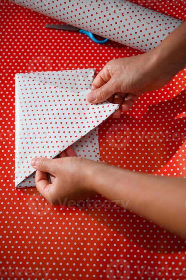 Close-up of hands wrapping a gift in red polka dot paper for a festive occasion, capturing the joy and care involved in preparing a special present for holidays or celebrations photo