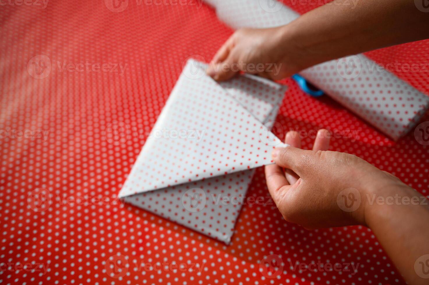 Hands carefully folding polka dot paper for gift wrapping on red dotted surface, showcasing attention to detail and creativity in preparing presents for special occasions or festive seasons. photo