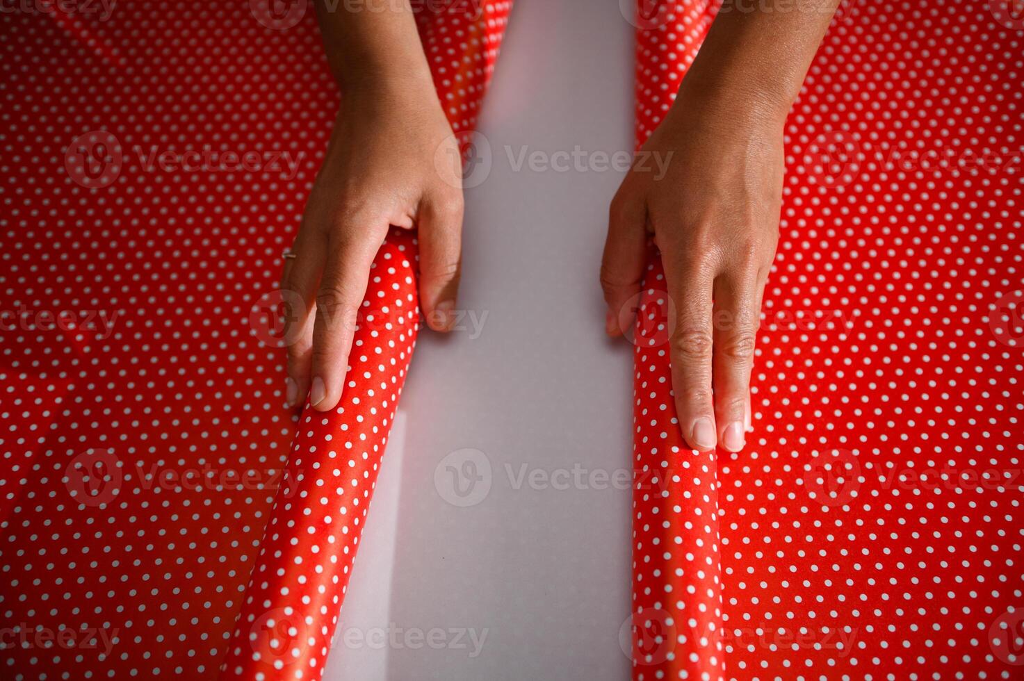 Hands carefully folding vibrant red polka dot wrapping paper, preparing for gift wrapping during a festive occasion or special celebration photo