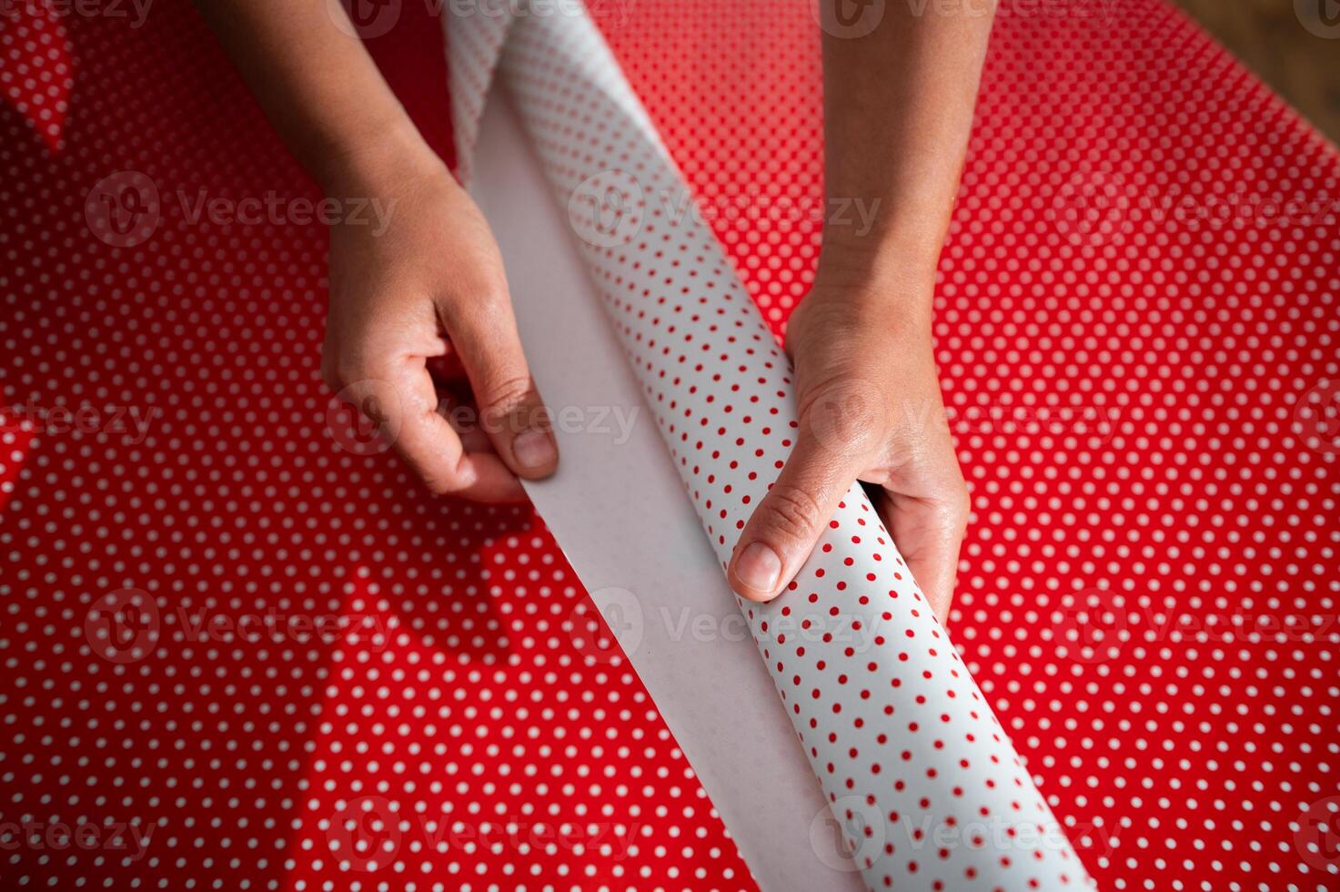 Hands wrapping a gift with red and white polka dot paper, focusing on the holiday spirit and creativity photo