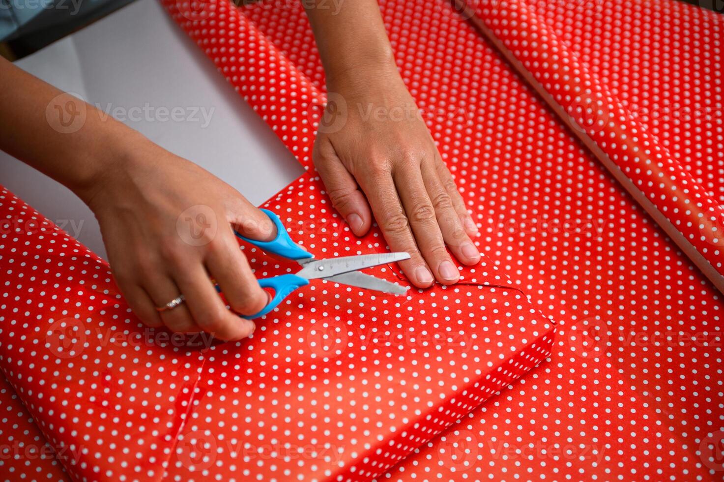 Hands using scissors to cut festive red and white polka dot wrapping paper, preparing for gift wrapping occasion such as Christmas or birthdays in a creative and organized manner. photo
