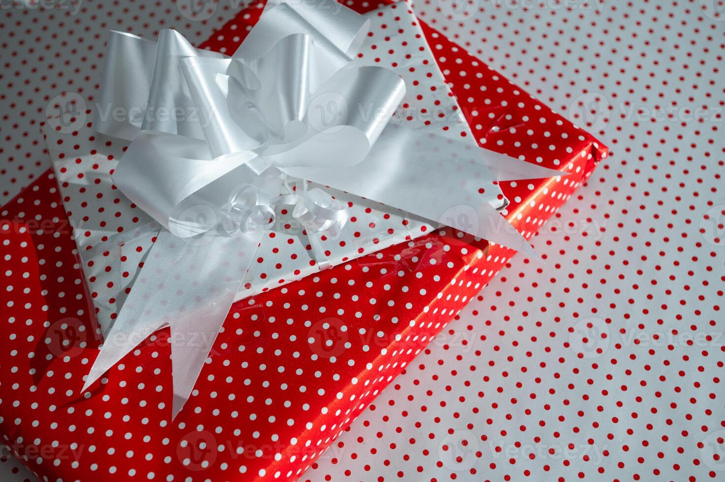 Festive gift box with a vibrant red polka dot pattern and elegant white ribbon resting on matching dot background photo