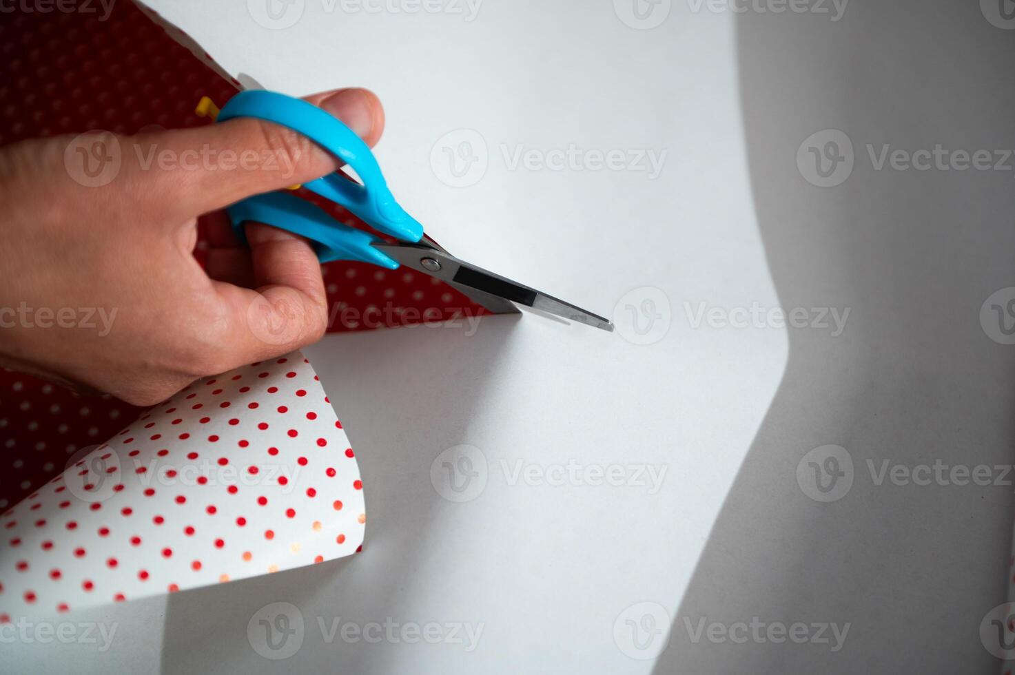 Cutting wrapping paper with blue scissors creating polka dot gift wrap during holiday season photo