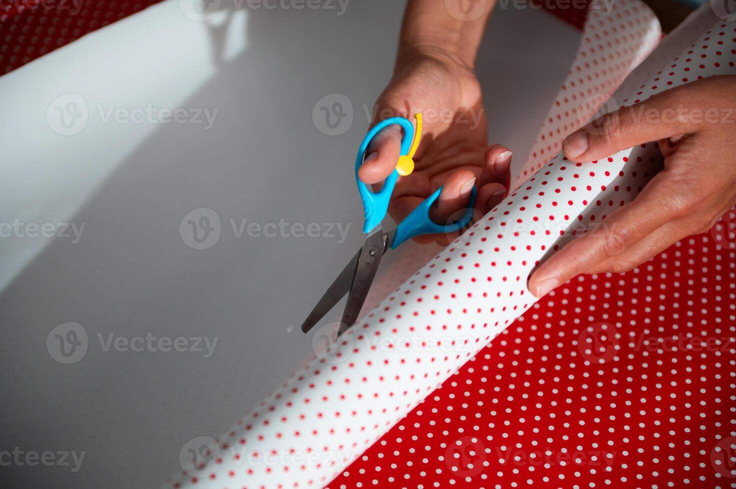 Hands meticulously cutting festive wrapping paper with scissors on a table, enhancing gift preparation for holiday celebrations photo