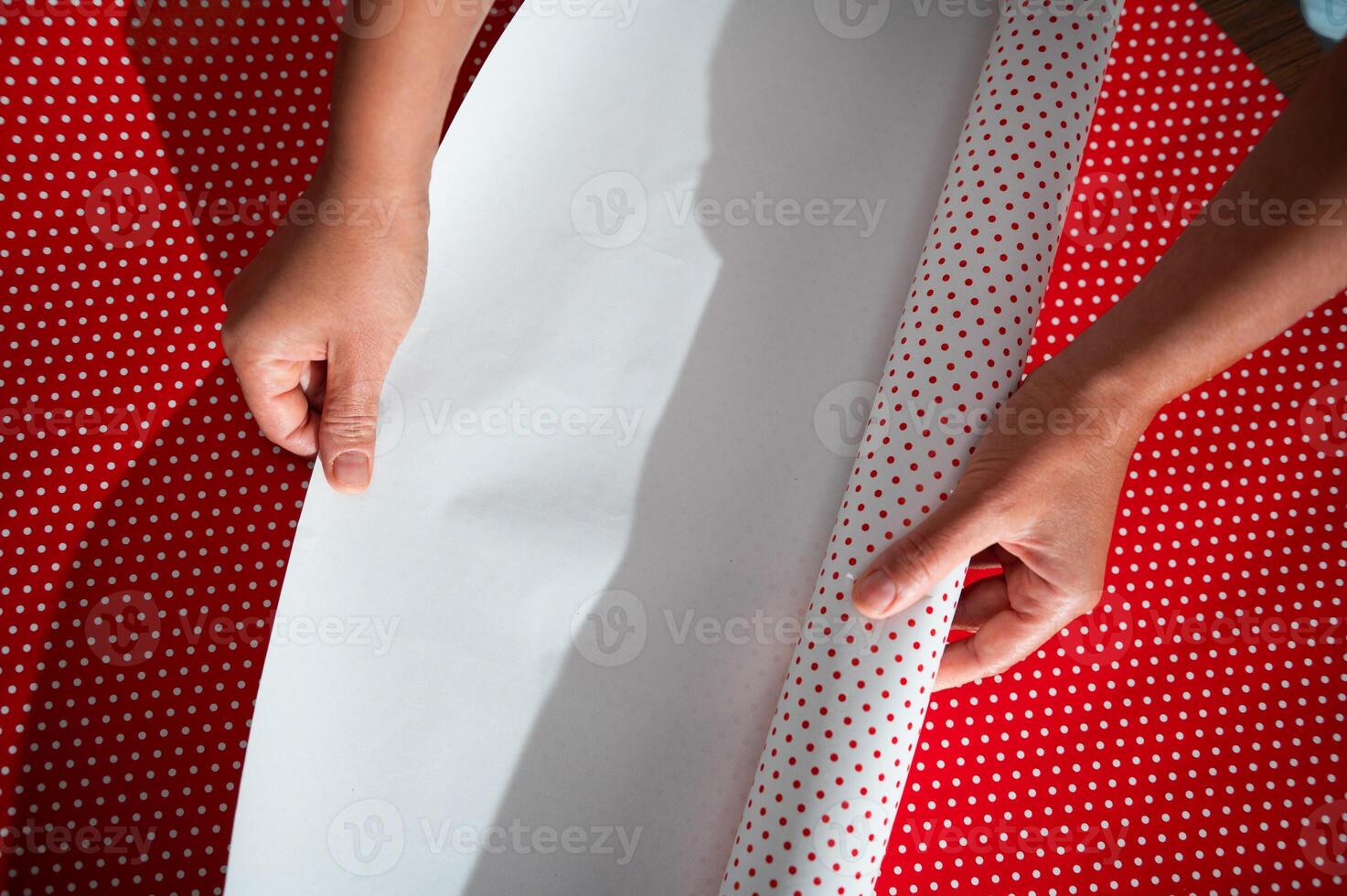 Hands wrapping gift with red and white polka dot paper, showcasing holiday preparation and festive cheer photo