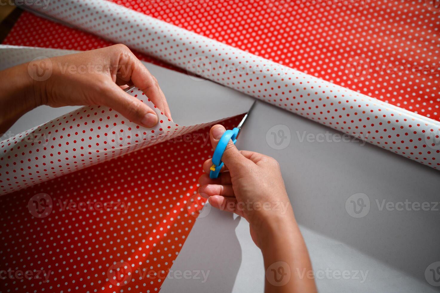 Person wrapping a gift with red and white polka dot wrapping paper using scissors photo
