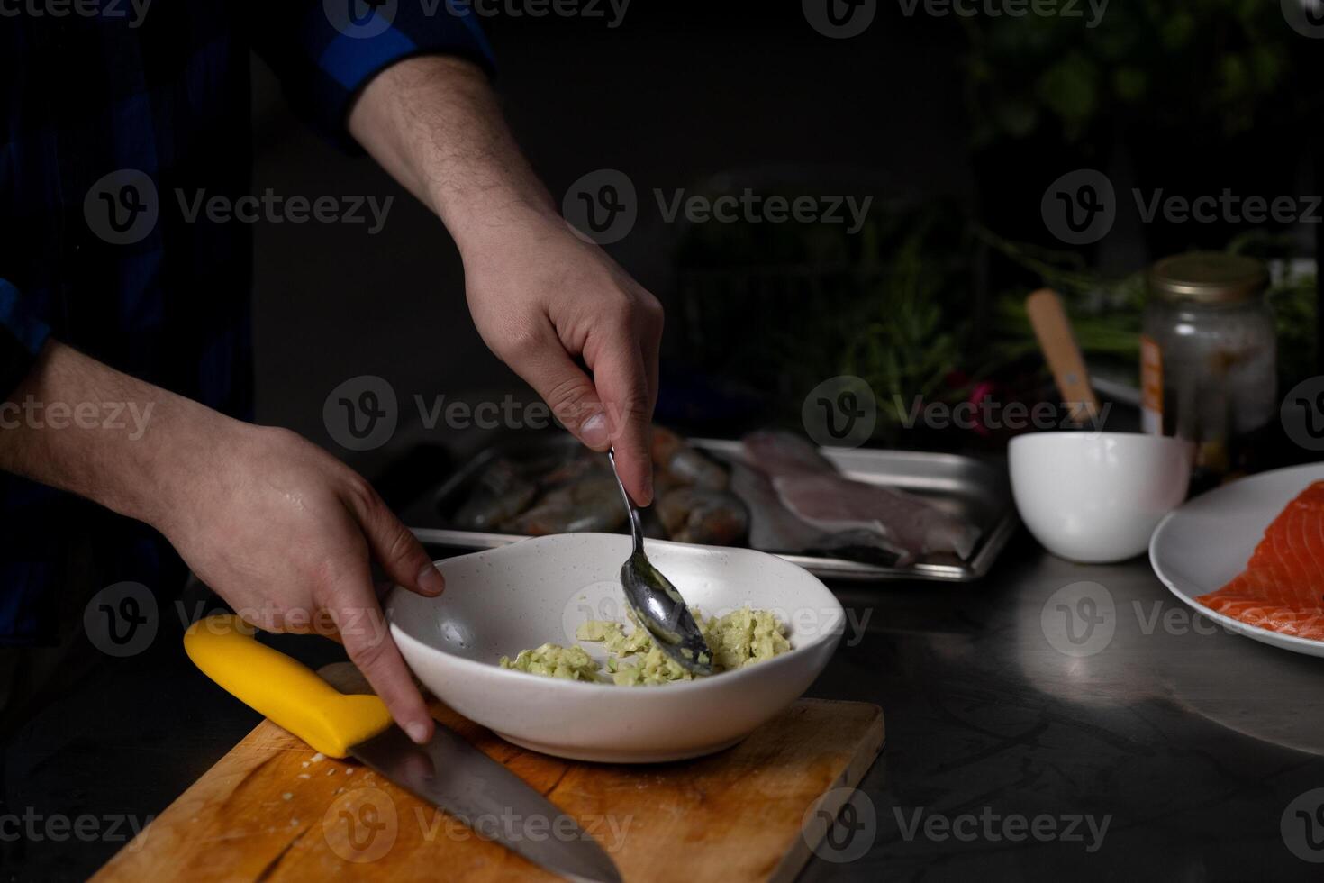 Person mixing fresh ingredients in bowl. Kitchen setting includes various food items and utensils, indicating active meal preparation photo