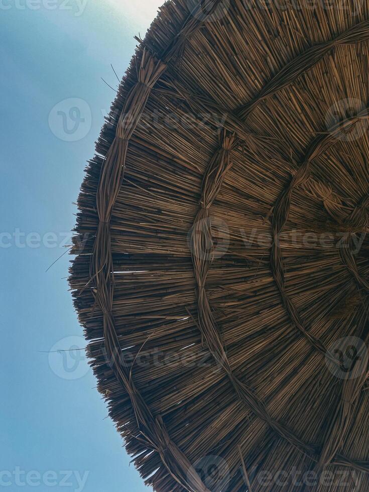 Straw parasol on clear blue sky background. Woven texture of natural fibers, evoking summer relaxation and beach vibes. Perfect for vacation and leisure designs photo