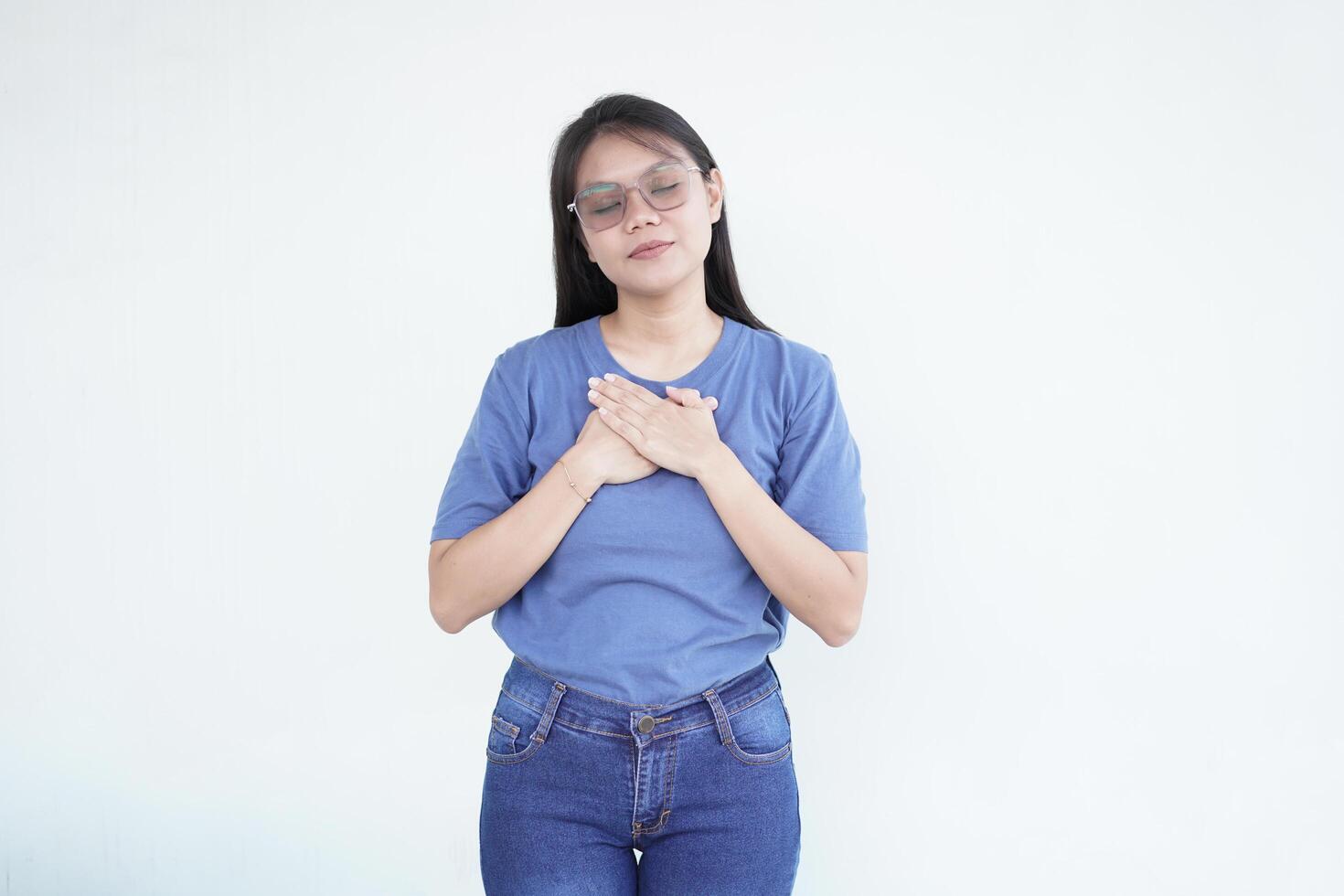 Beautiful Asian woman places her hand on her chest, symbolizing self-love and care, against a white background photo