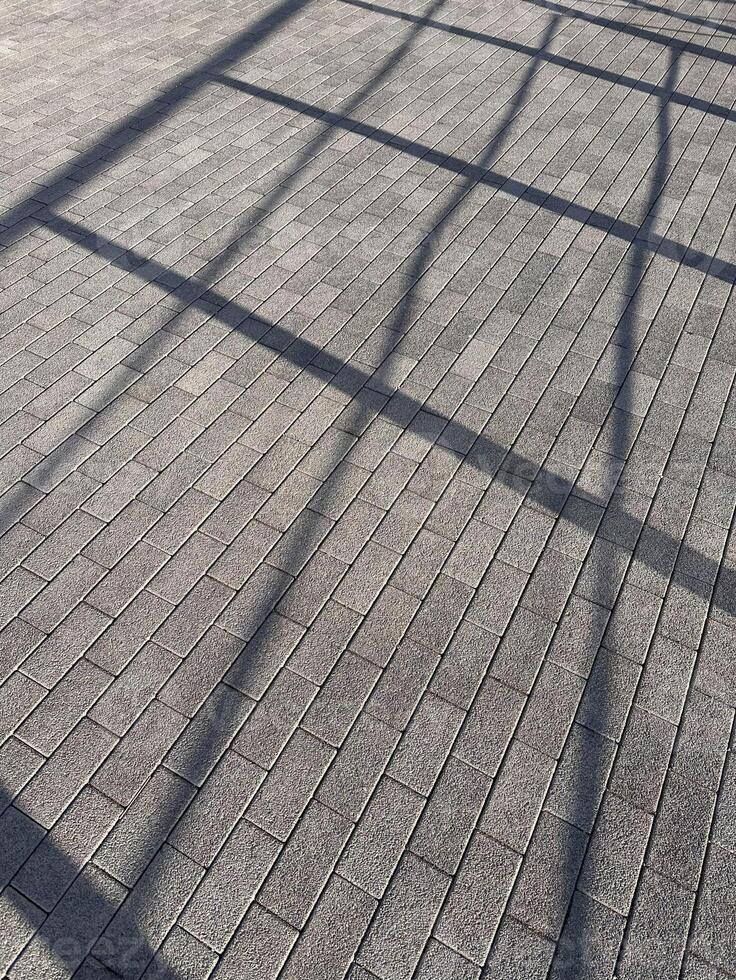 Shadow of metal fence on grey brick pattern pavement. Abstract background and texture. Sunlight,light and shadow concept photo