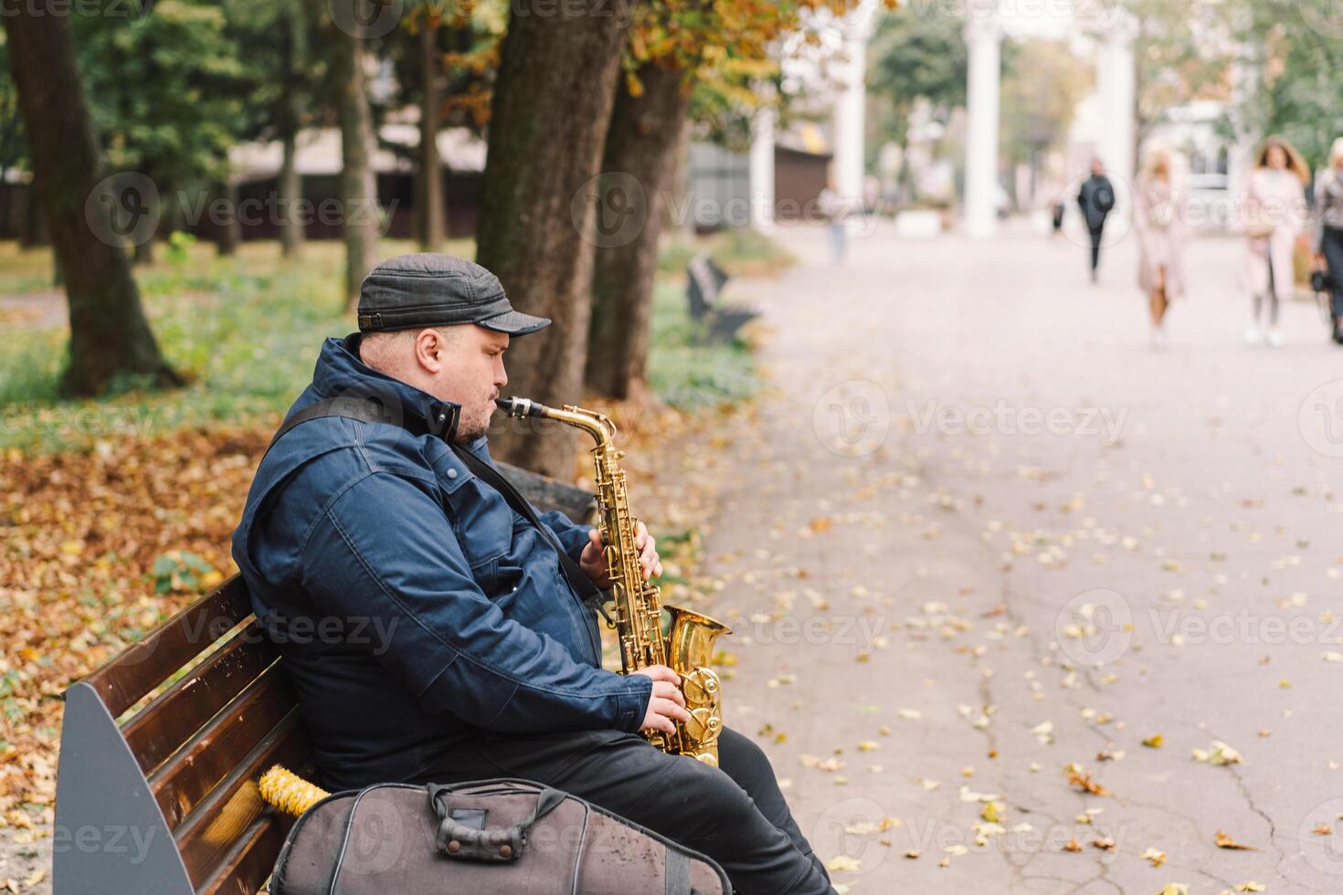 A saxophonist performs in a serene park during autumn while seated on a bench photo