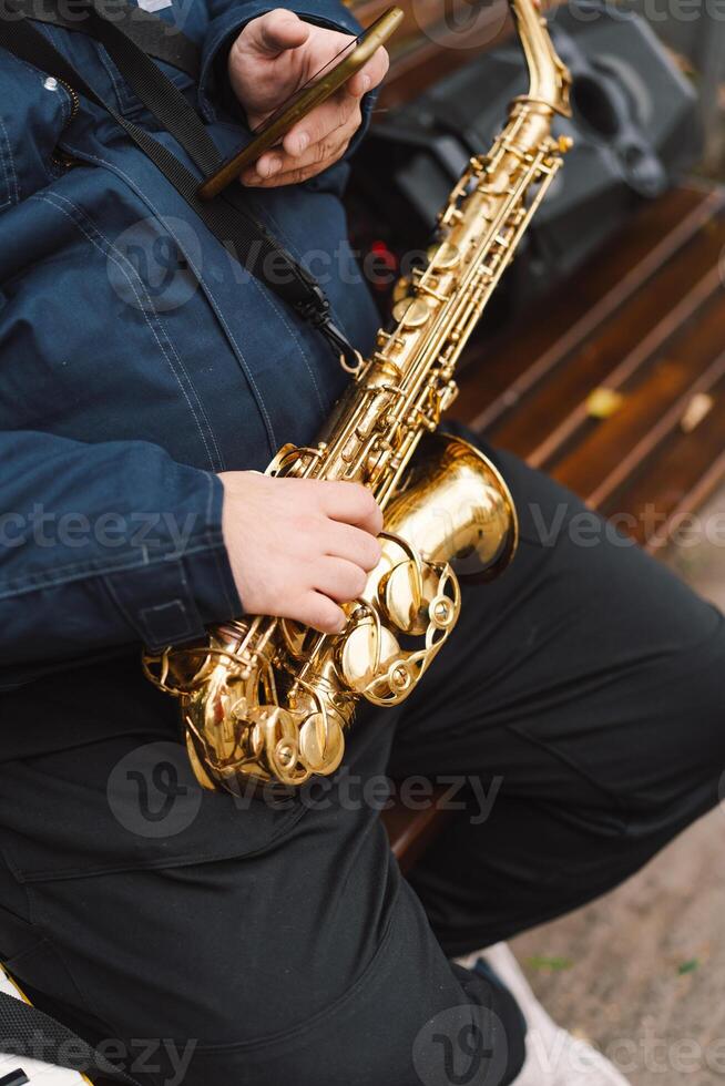 A saxophonist performs in a serene park during autumn while seated on a bench photo