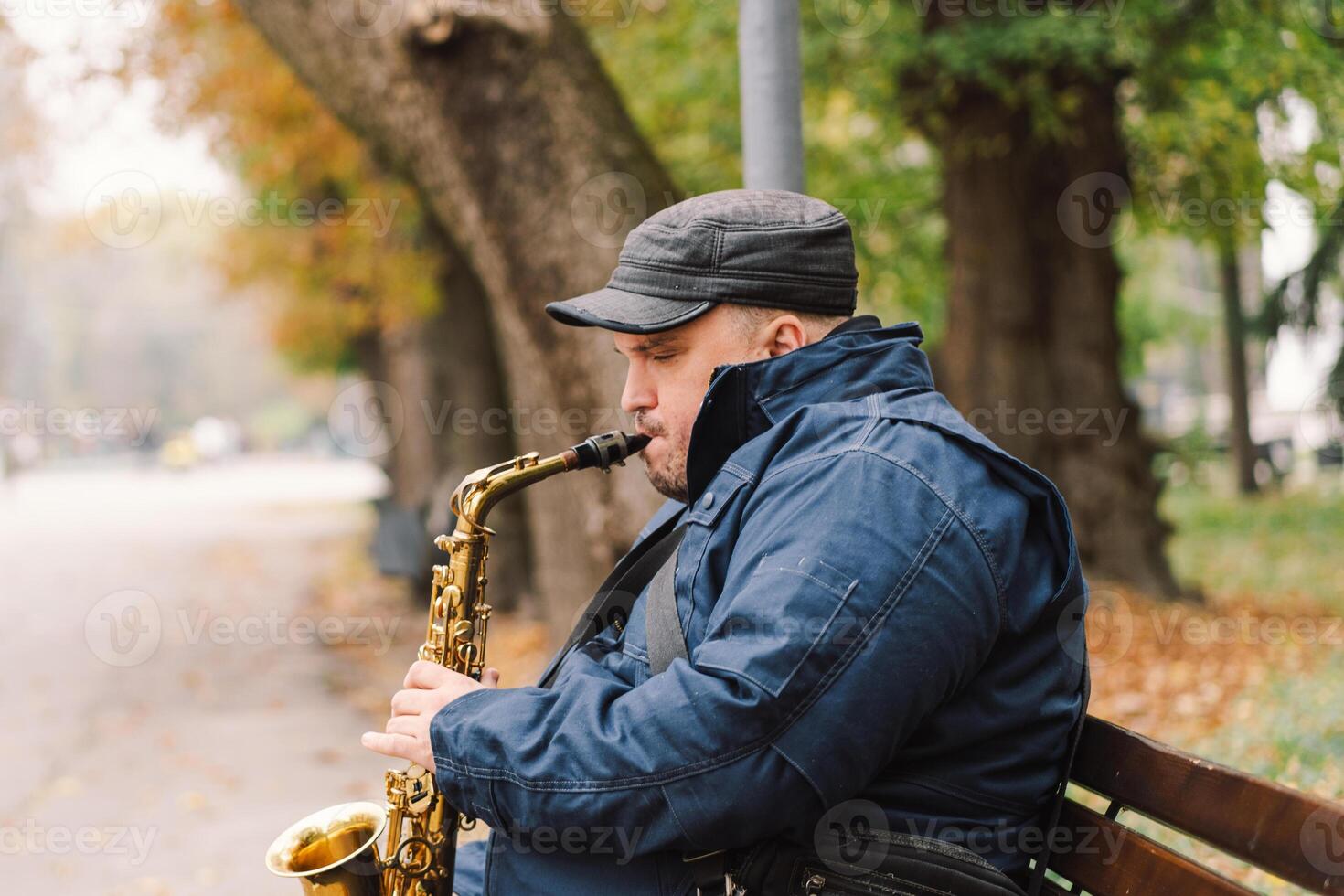 A saxophonist performs in a serene park during autumn while seated on a bench photo