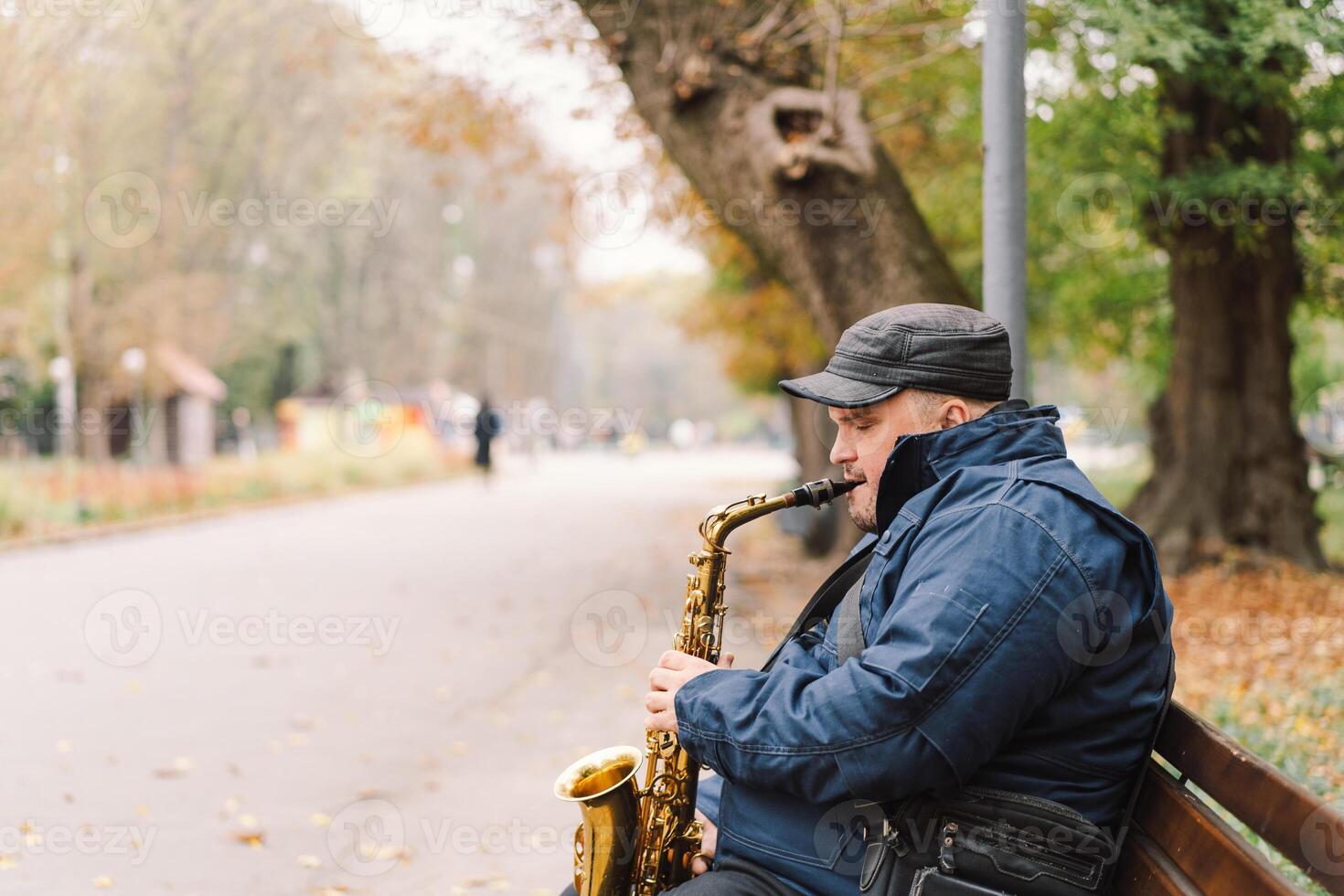A saxophonist performs in a serene park during autumn while seated on a bench photo