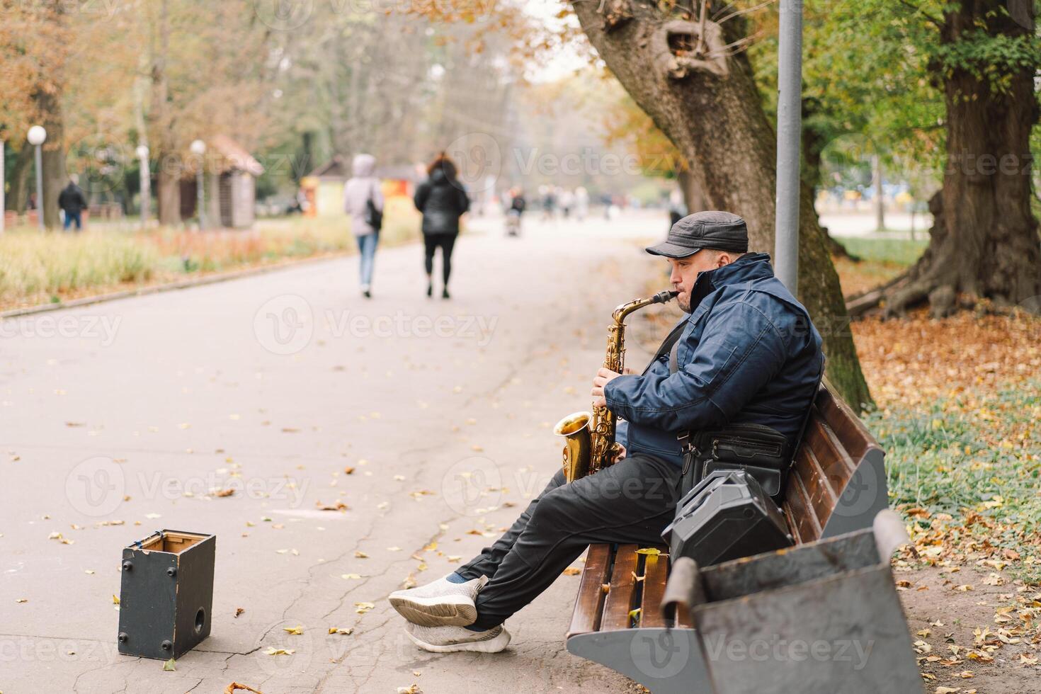 A saxophonist performs in a serene park during autumn while seated on a bench photo