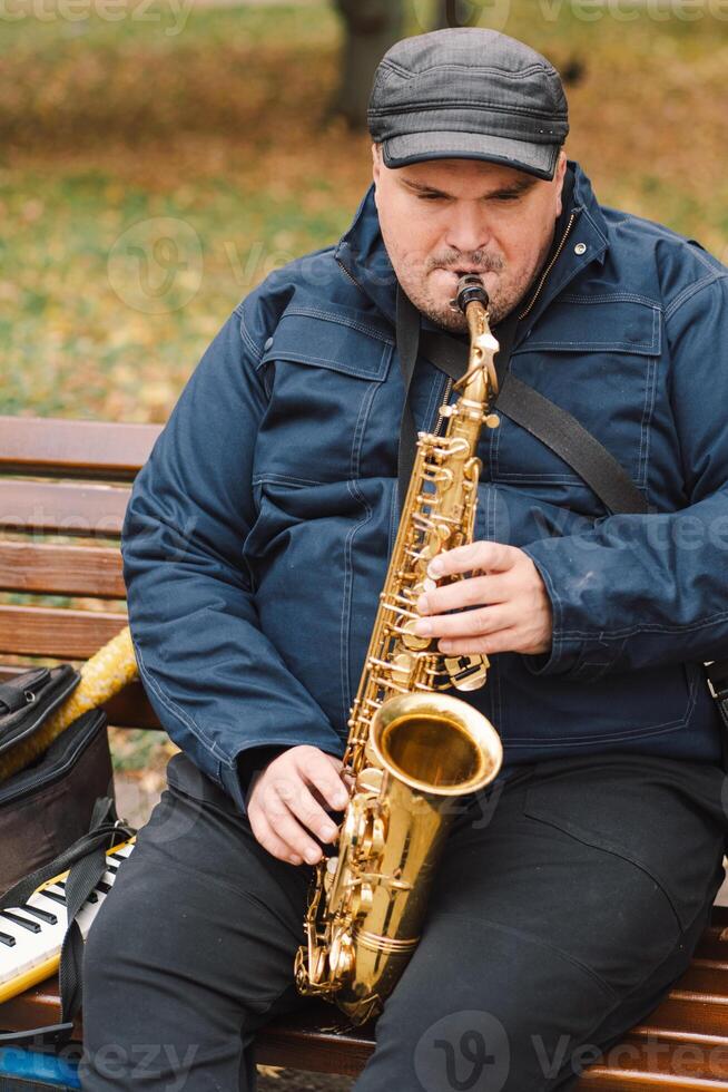 A saxophonist performs in a serene park during autumn while seated on a bench photo