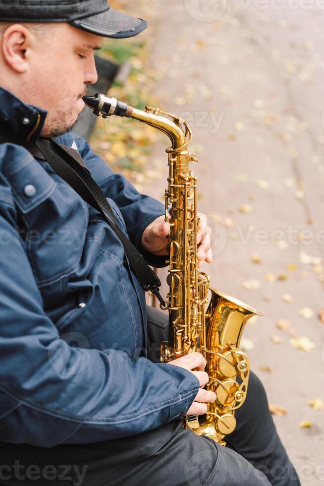 A saxophonist performs in a serene park during autumn while seated on a bench photo