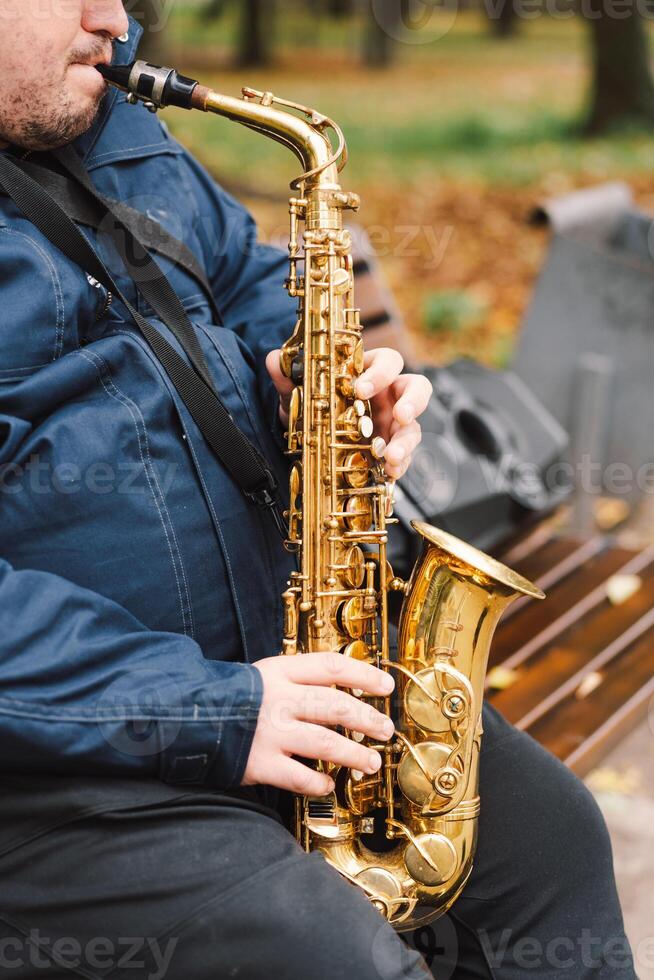 A saxophonist performs in a serene park during autumn while seated on a bench photo