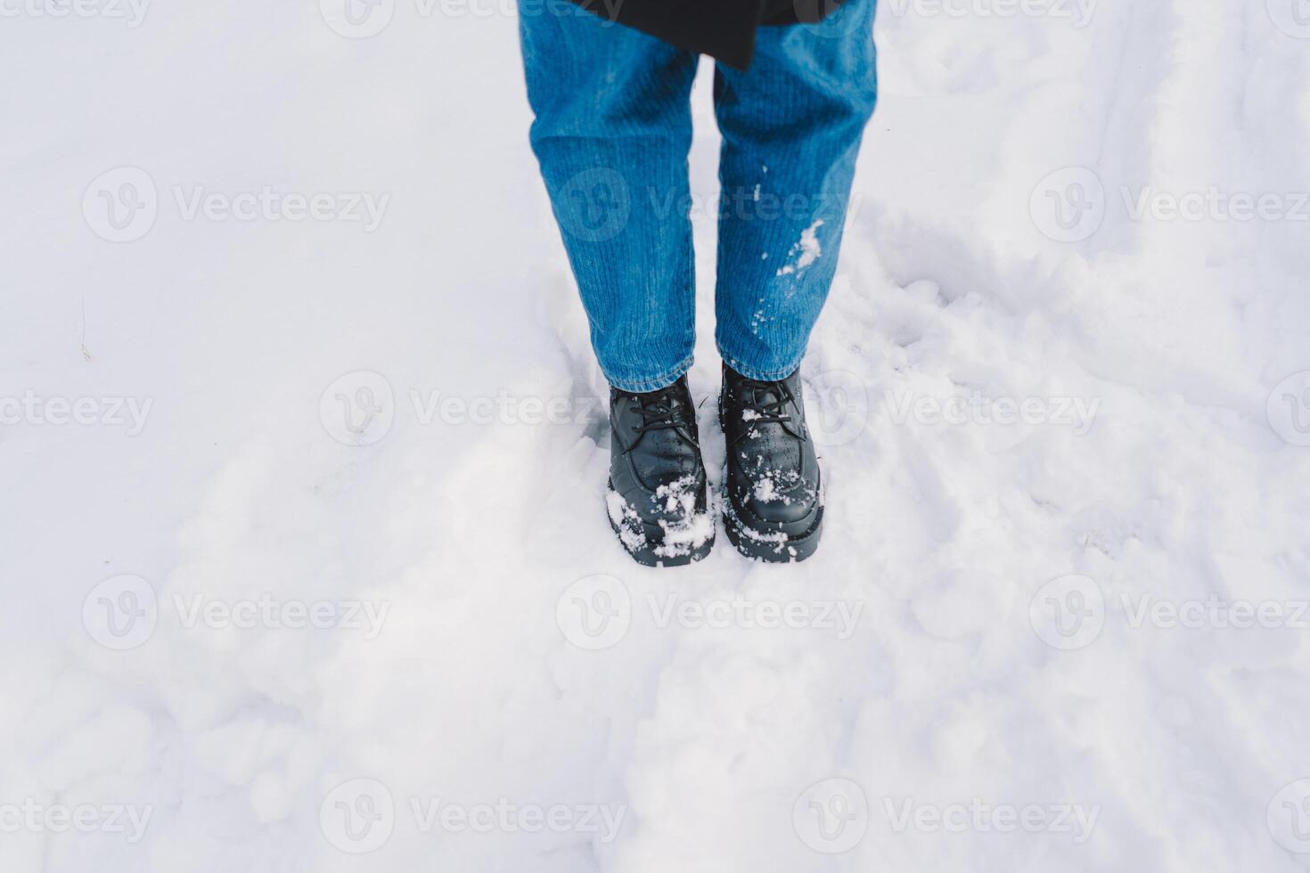 Woman standing in fresh snow wearing black boots and blue jeans during a winter day photo