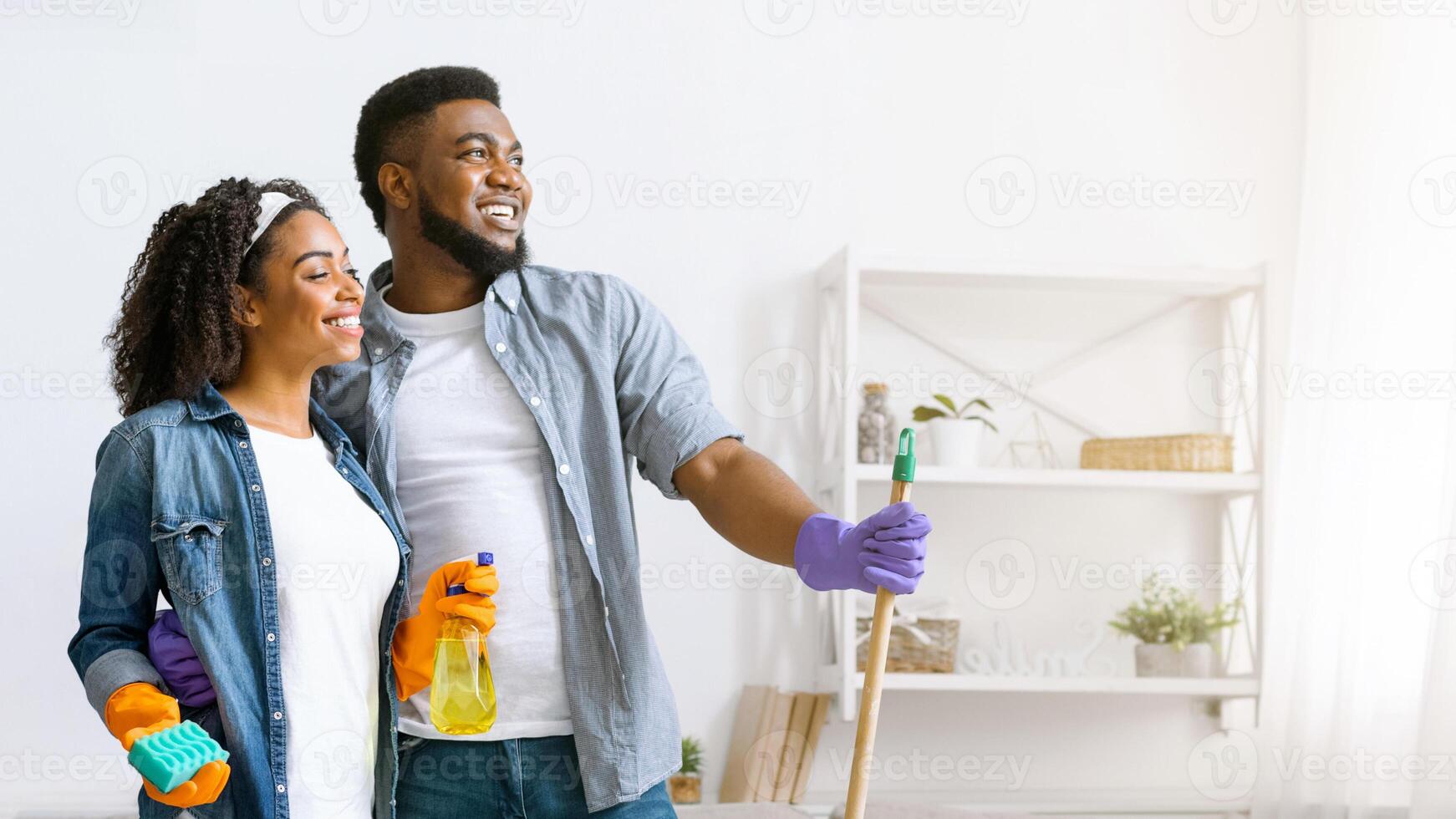 Happy Black Couple Standing In Fresh-Cleaned Living Room And Looking Aside, Satisfied After Successful Tidying, Copy Space photo