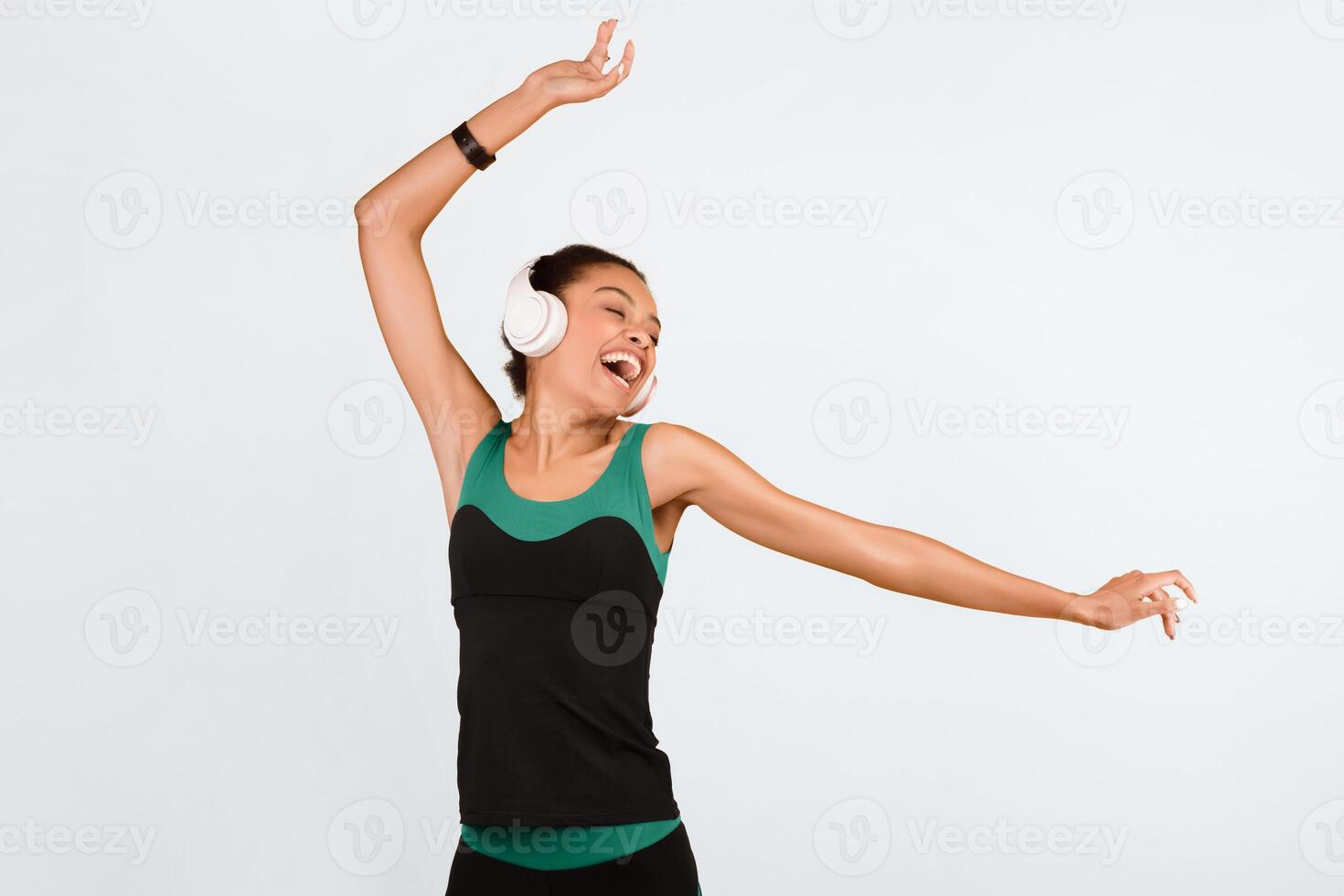 Black Sporty Girl In Wireless Earphones Listening To Music Dancing And Singing Over Yellow Studio Background. photo