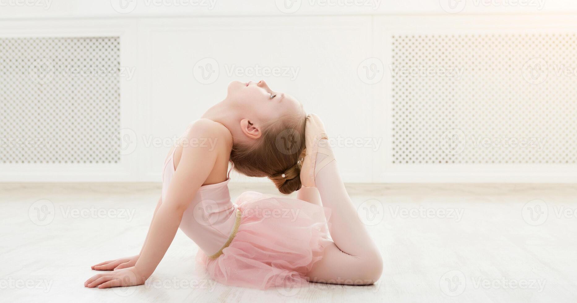 Little ballerina in split on floor, copy space. Smiling baby girl dreaming to become professional ballet dancer, classical dance school photo