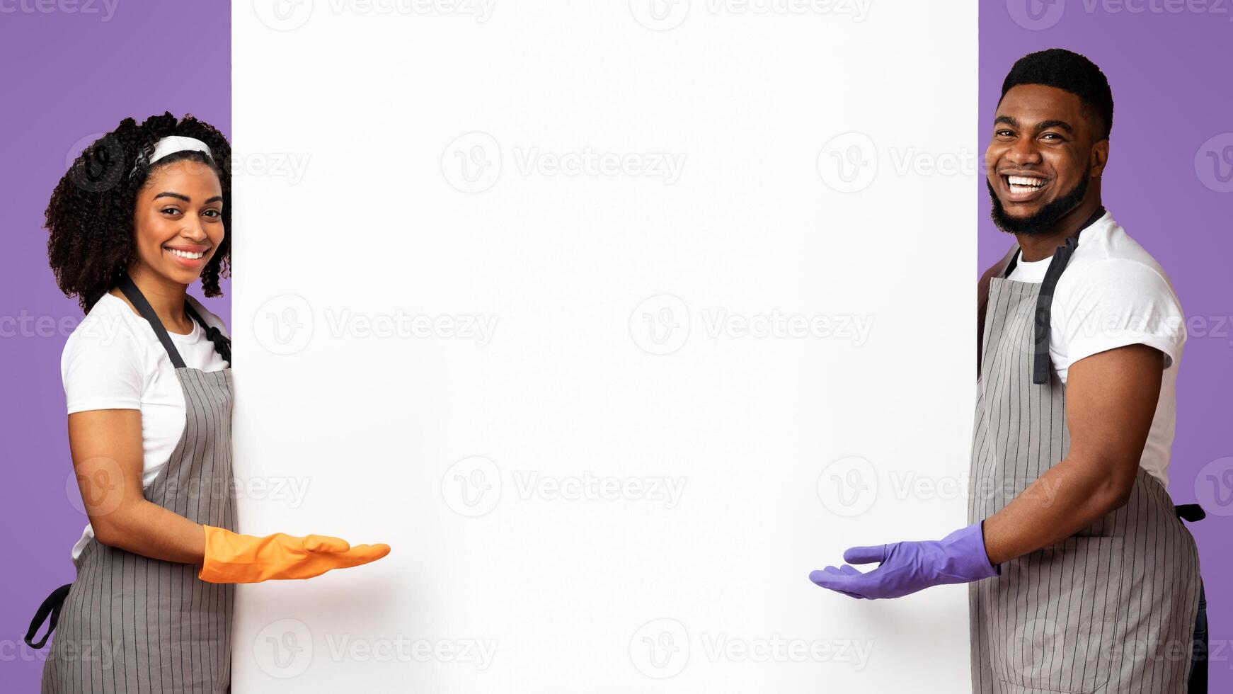 Spring Cleaning Ad. Positive African Couple In Rubber Gloves And Aprons Pointing At White Advertisement Board With Copy Space For Your Text, Panorama photo