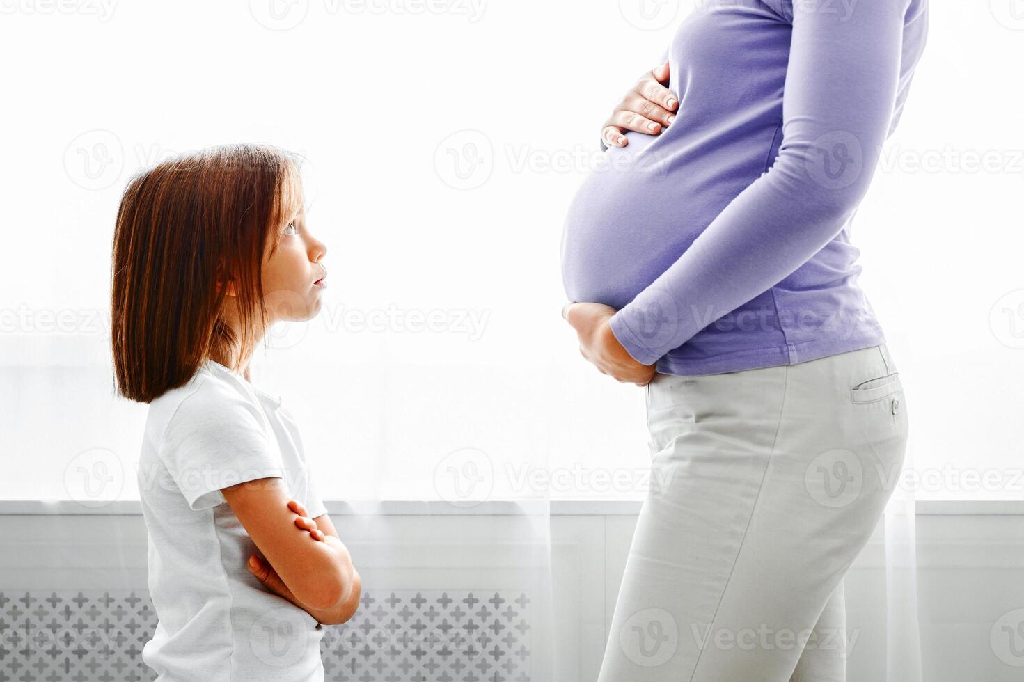 Little daughter looking at her expecting mother with reproach, side view, close up photo