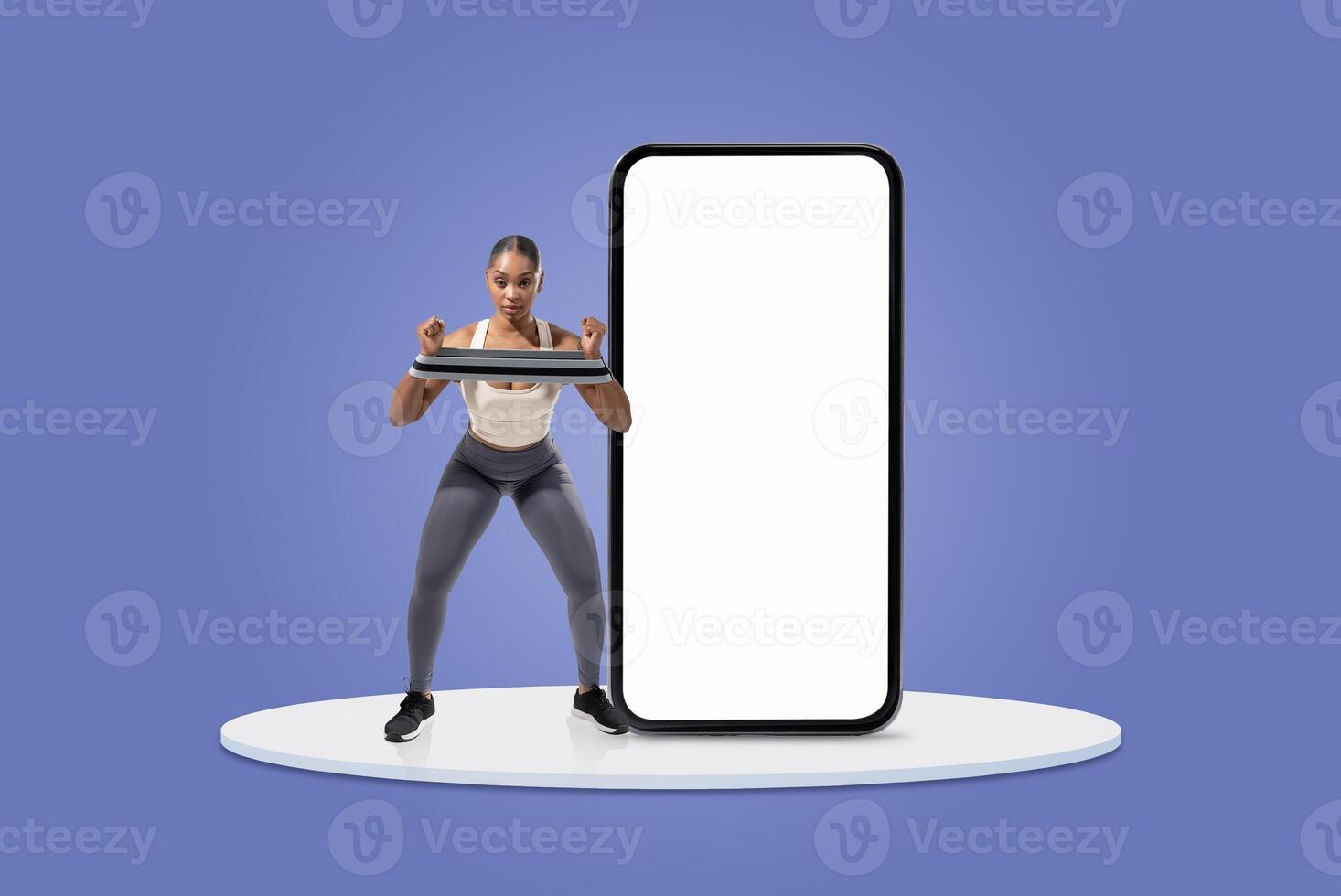 A woman performs strength training with a resistance band while positioned in front of a large blank screen. She appears focused and engaged in her workout routine. photo