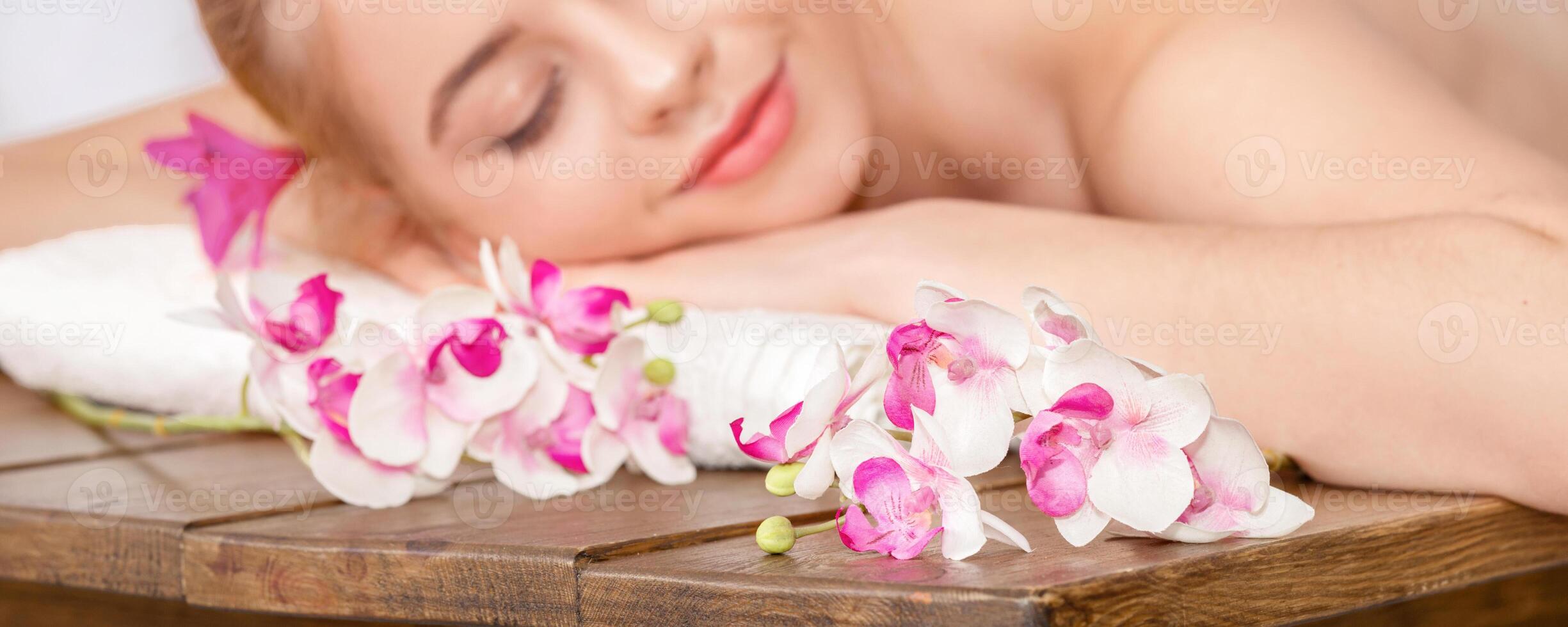 Pleasure of spa treatments. Female hands do relaxing massage for woman with closed eyes on table with orchids, close up photo