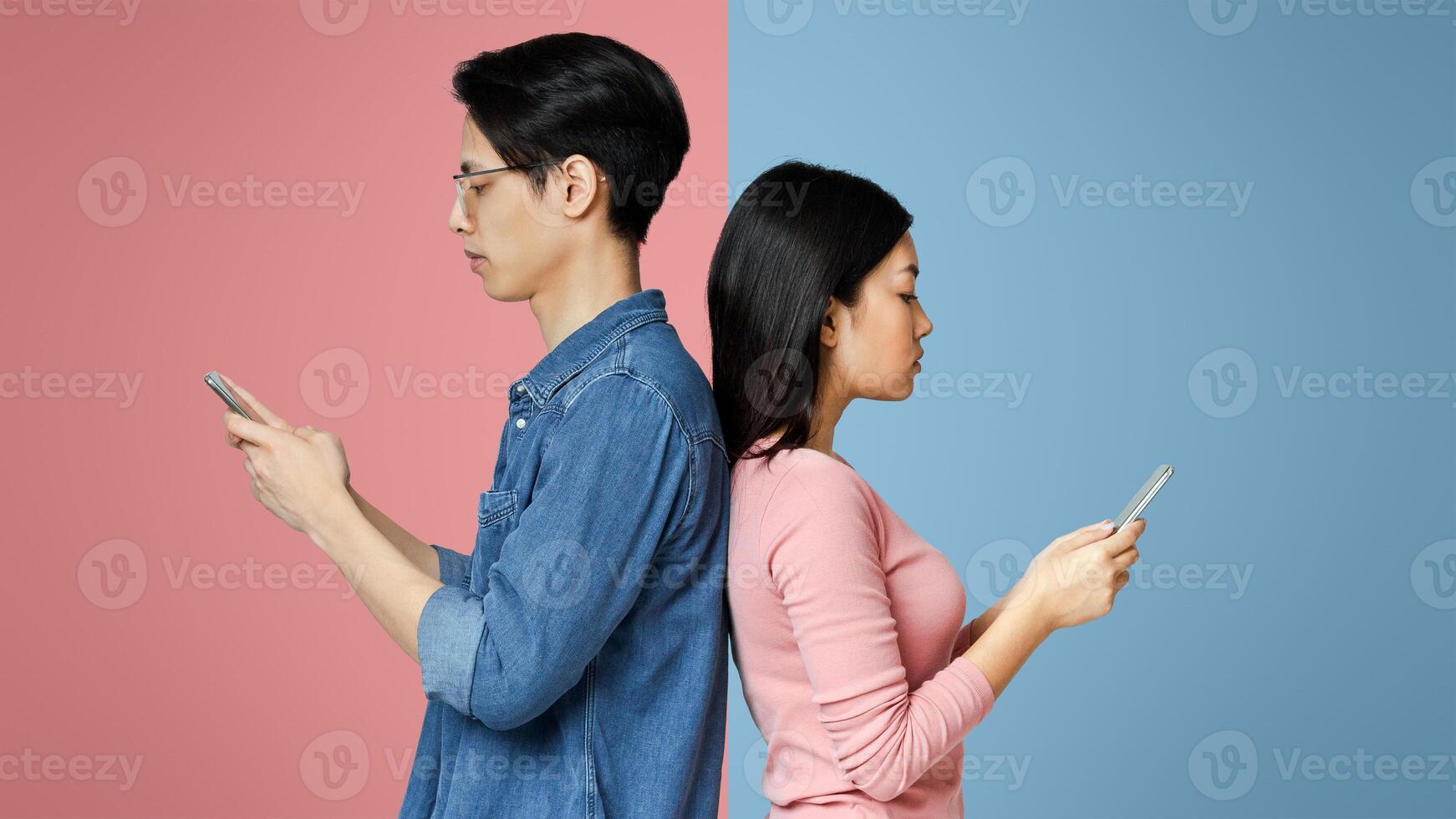 Asian girl and guy standing back to back, using mobile phones during quarantine, grey studio background photo
