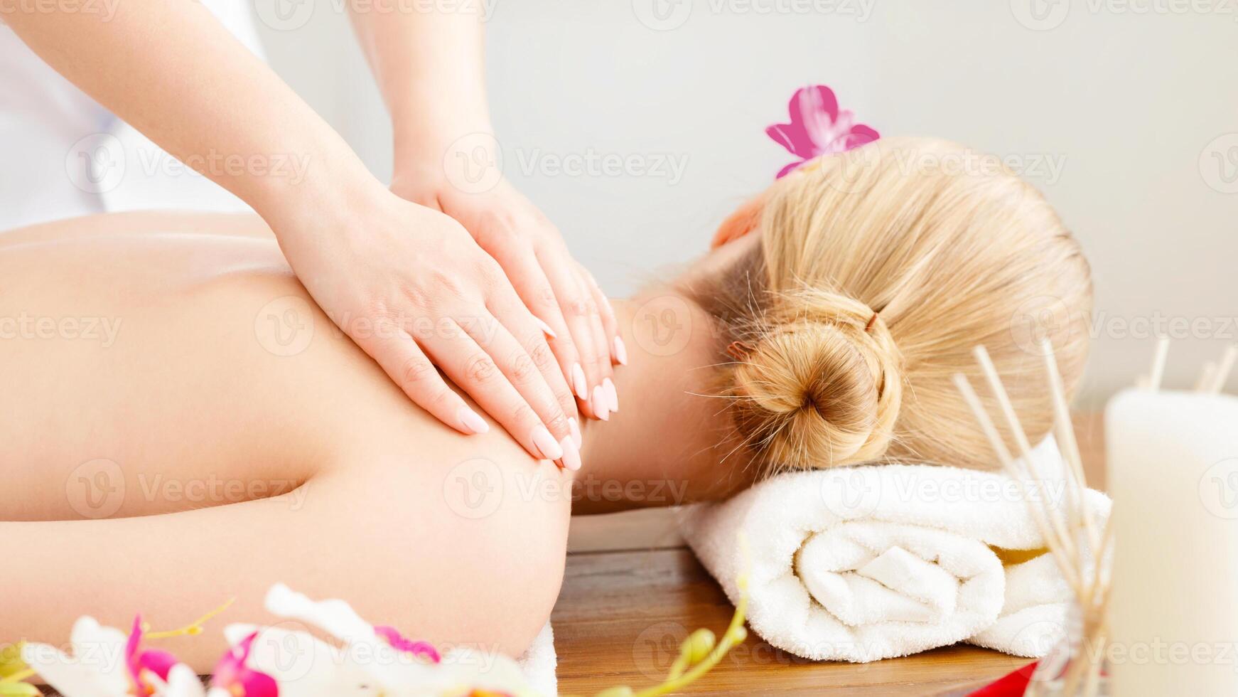 Female hands do massage on girl shoulders, lying on table with white towel, near orchid and aroma candles photo